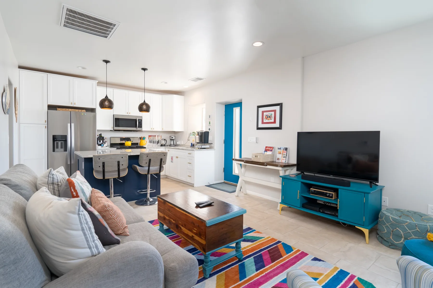 A bright living room opens onto a white kitchen, with a sofa and television.