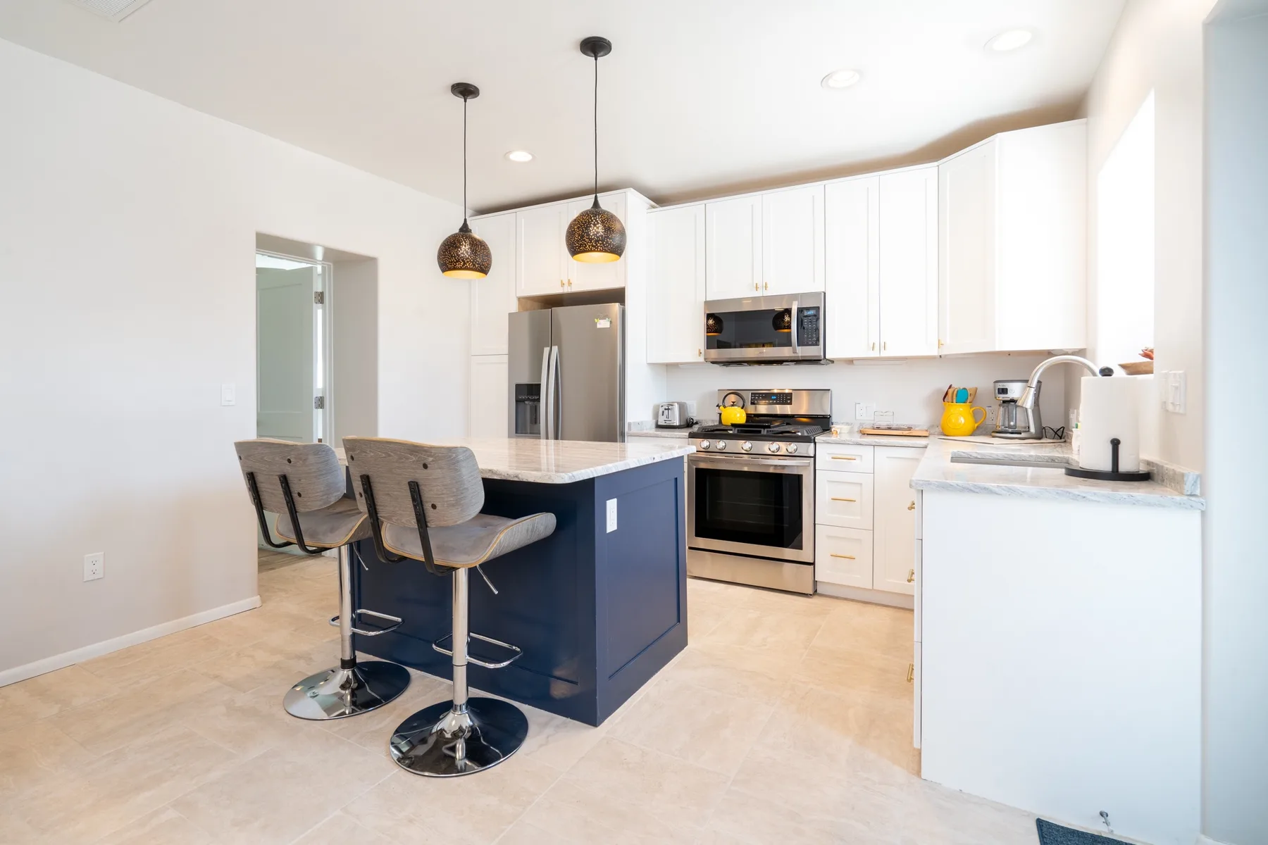 A bright kitchen with white cabinets, stainless steel appliances, and a dark island.