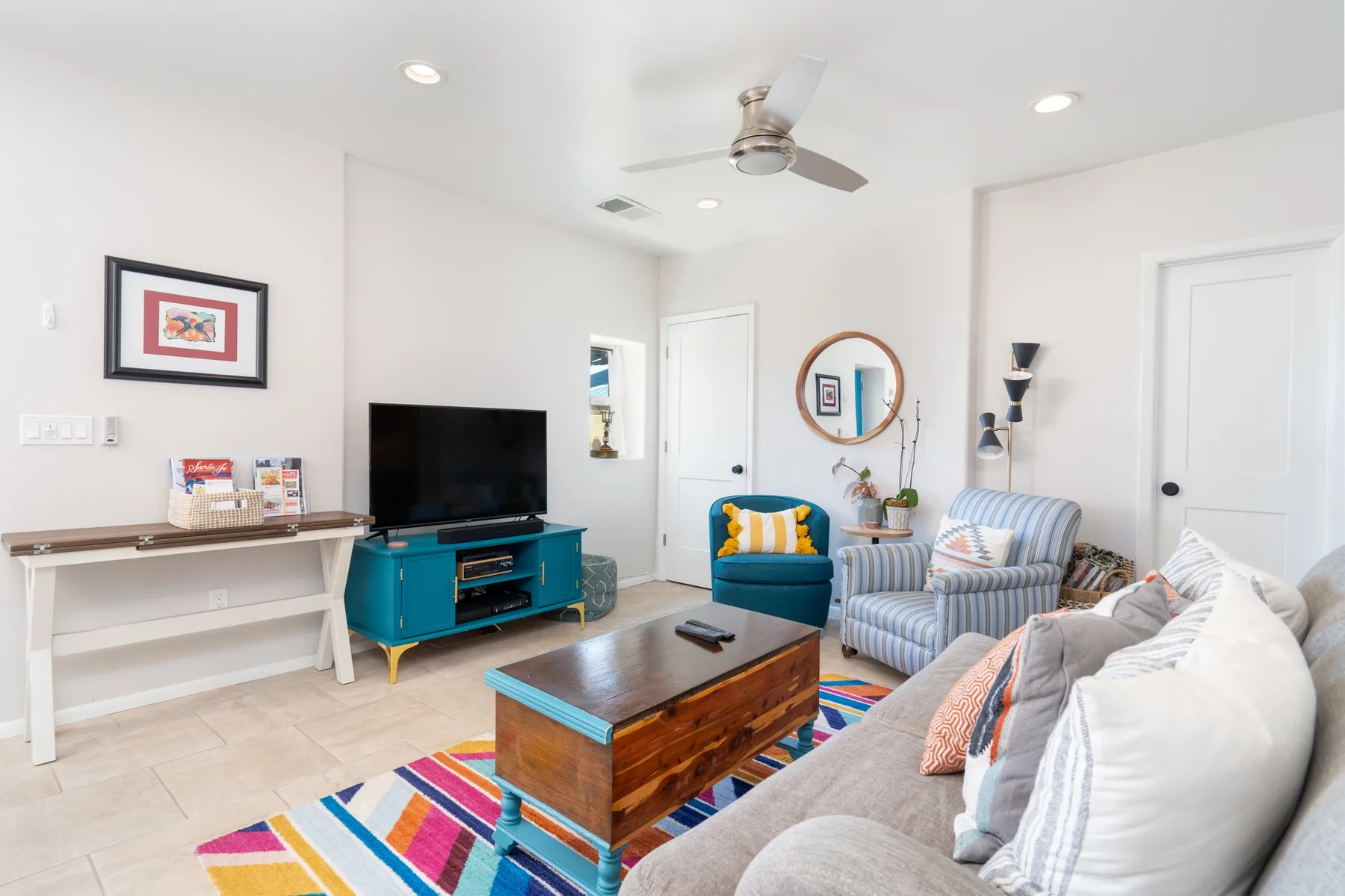 A bright living room with seating, a television, and a colorful rug.