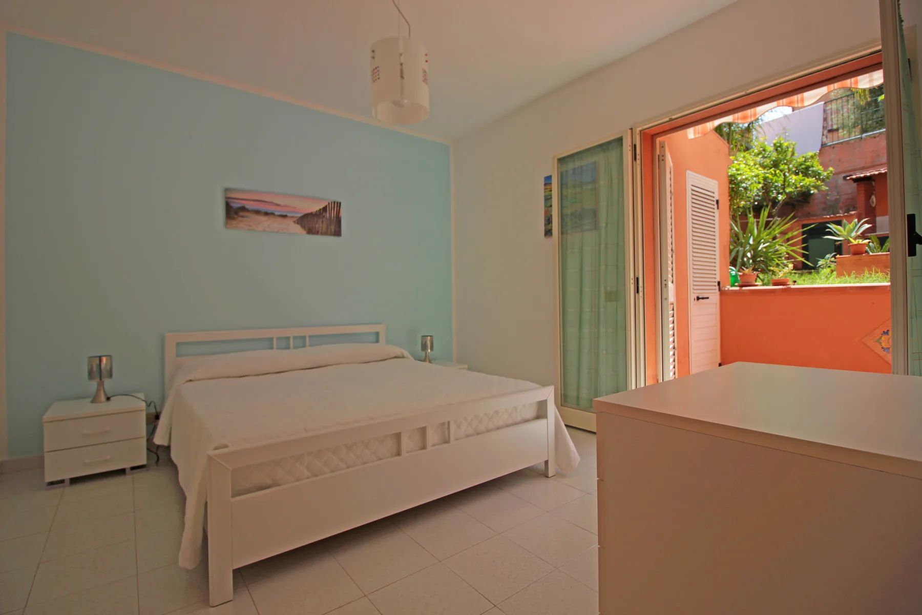 A bedroom with a bed beside an open doorway to a small outdoor patio.