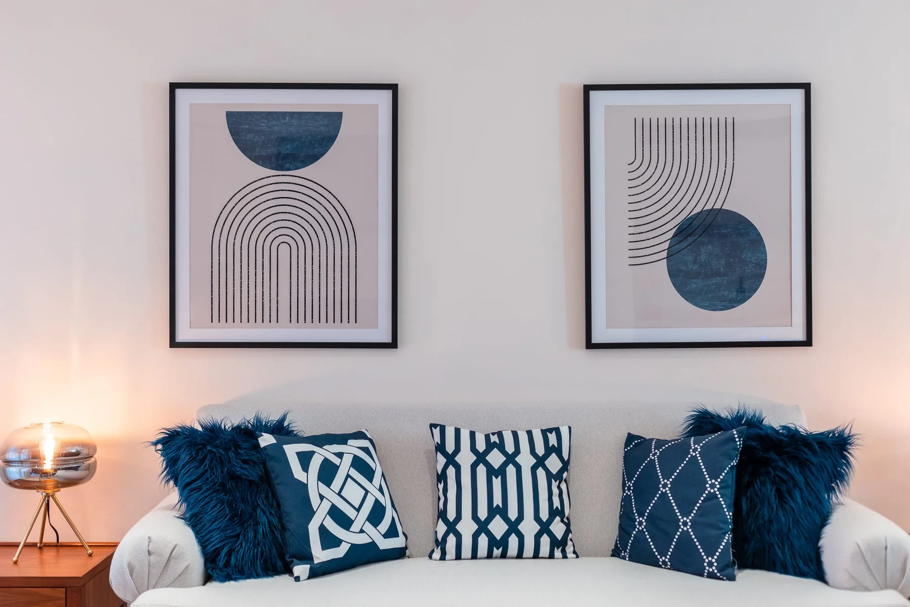 Zona de estar de una sala con cojines azules bajo dos láminas enmarcadas.