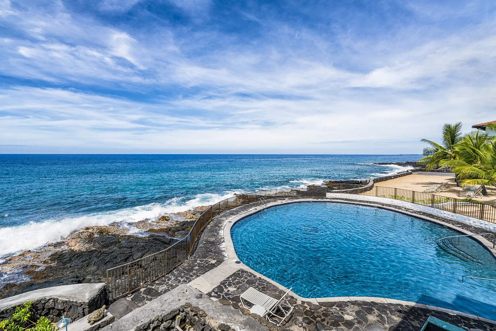Una piscina junto al océano, con palmeras a lo largo de la costa.