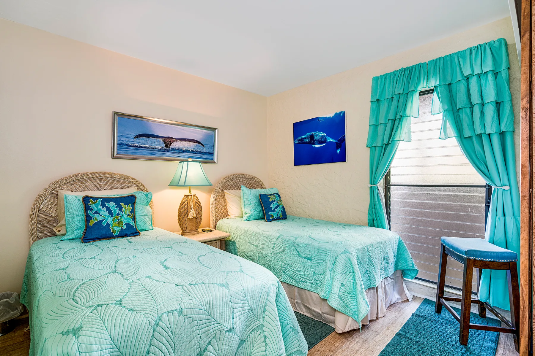 Un dormitorio con dos camas cubiertas de ropa turquesa junto a una ventana con cortinas.