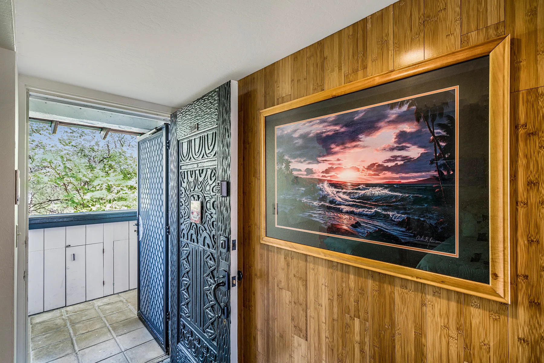 Una entrada revestida de madera presenta un paisaje marino al atardecer junto a una puerta decorativa abierta.