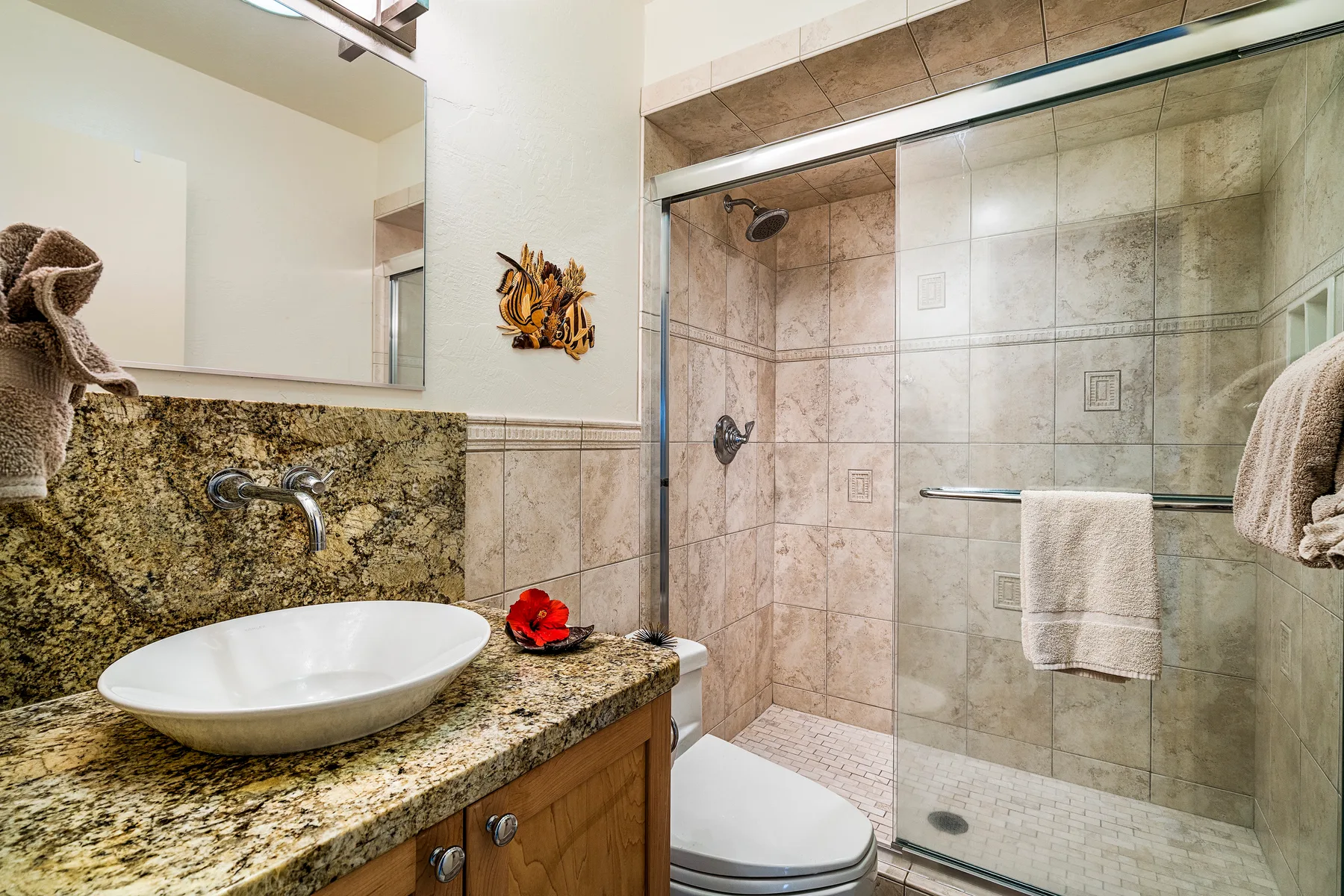 Un baño con lavabo de granito y una ducha con mampara de vidrio.
