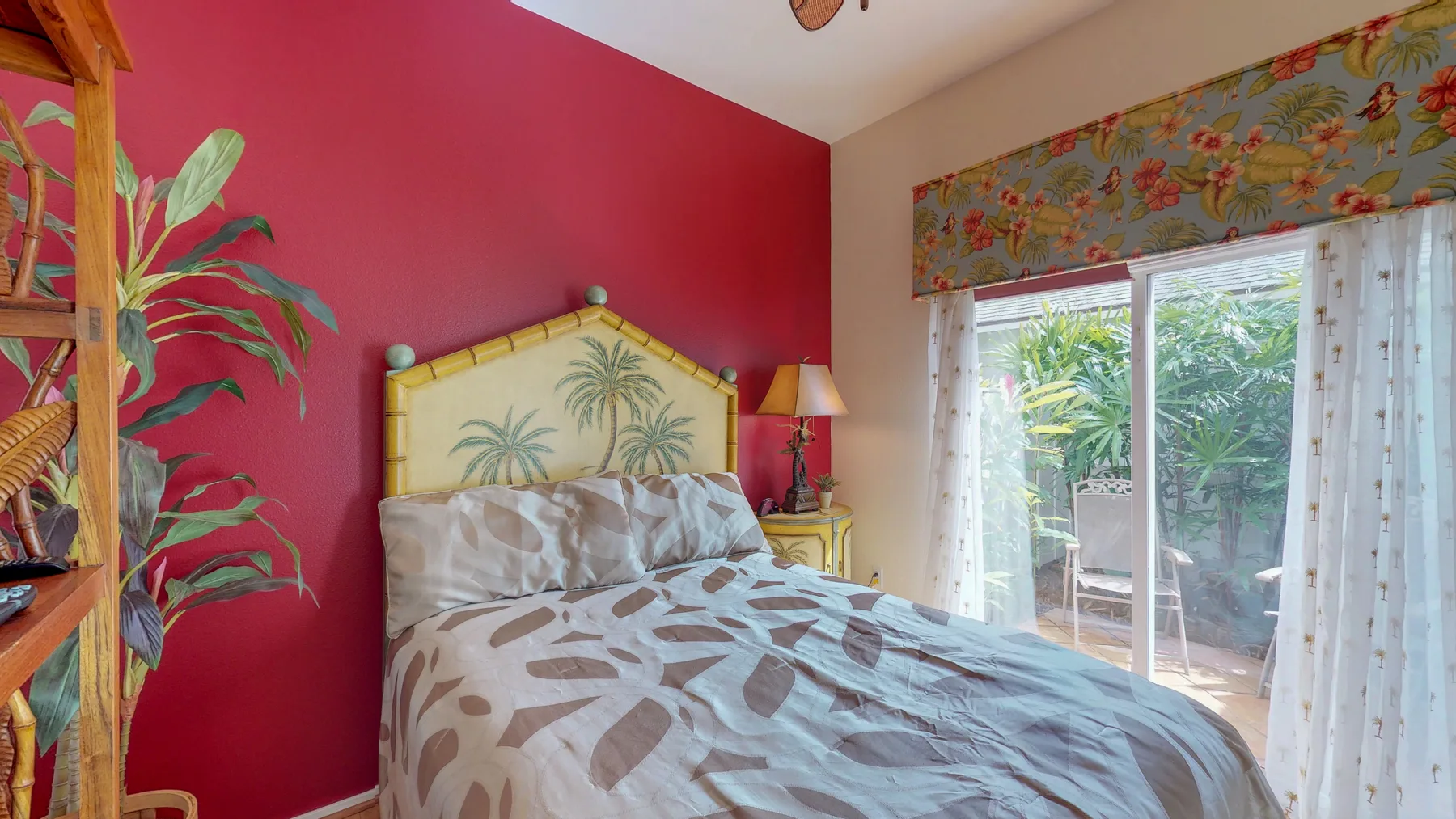 Un dormitorio con ropa de cama estampada y puertas corredizas de vidrio frente a la vegetación.