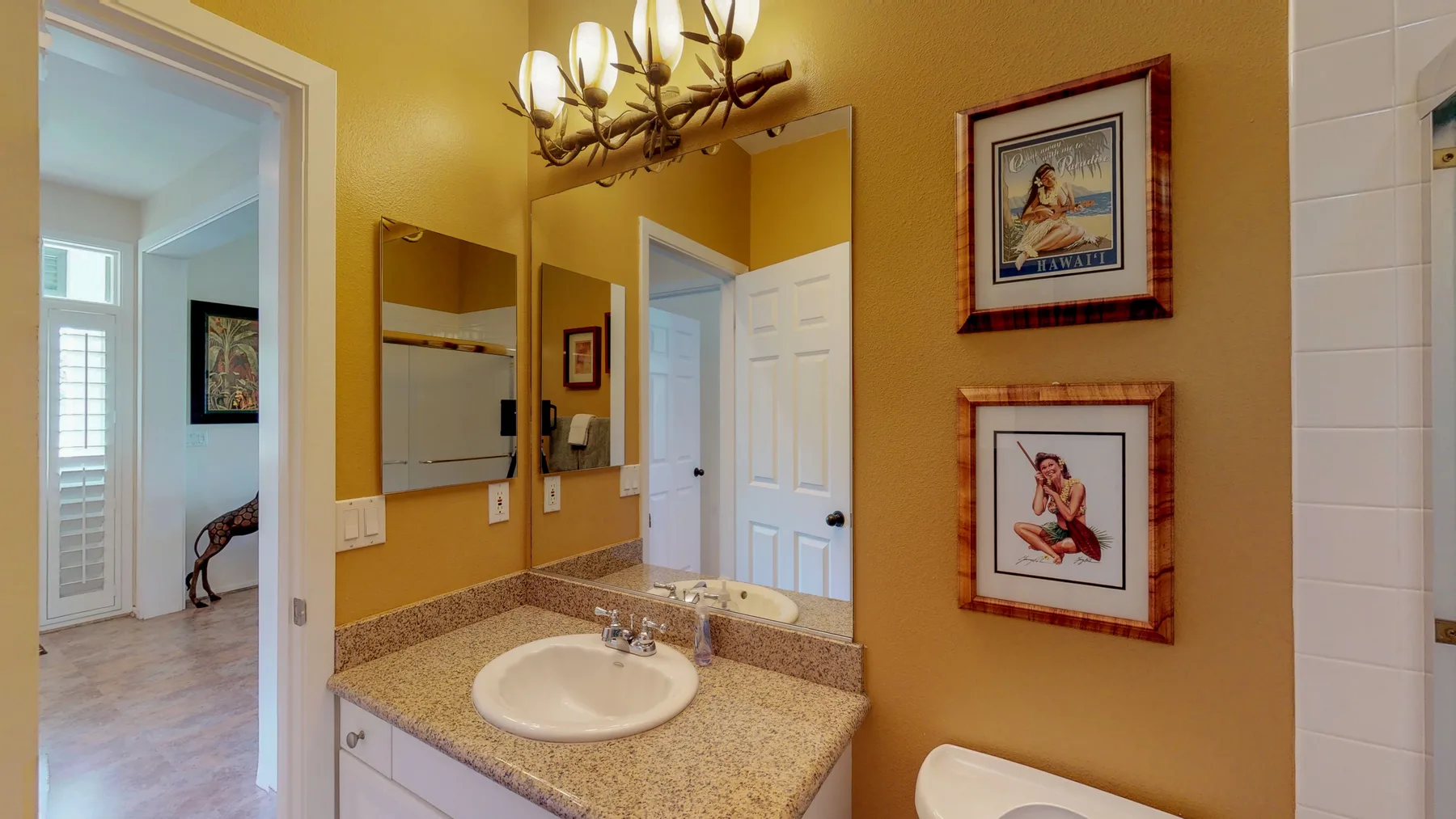 Un baño amarillo con lavabo, espejos de pared y cuadros enmarcados.