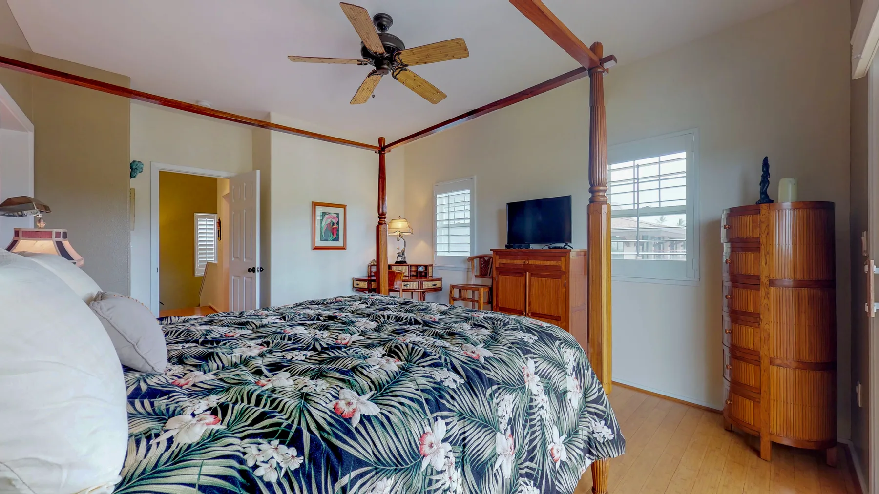 Un dormitorio con una colcha estampada, muebles de madera y ventanas.
