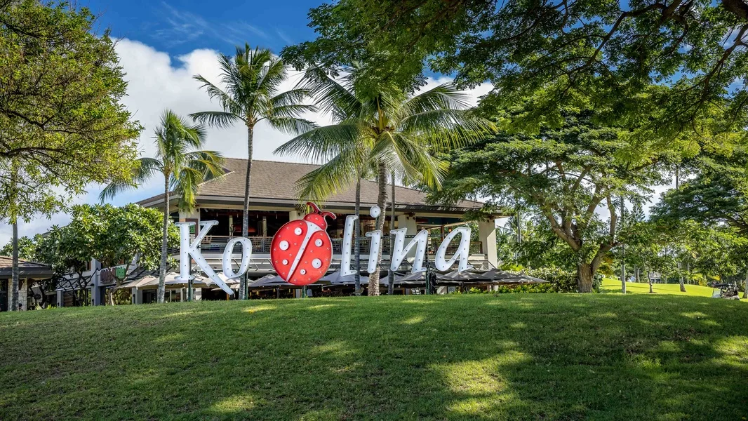 Un edificio de complejo tropical se alza detrás de un césped y palmeras.