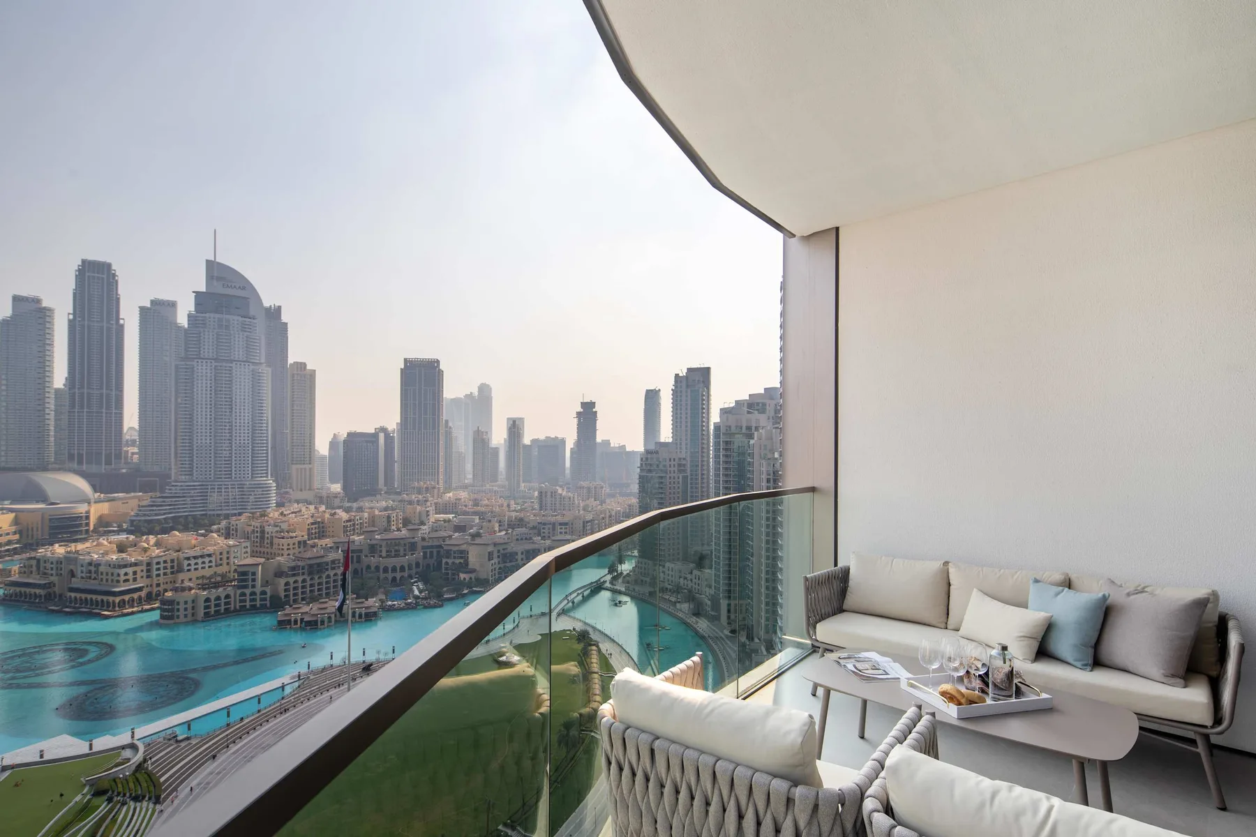 Una zona de estar en el balcón da a una piscina turquesa y al horizonte urbano.