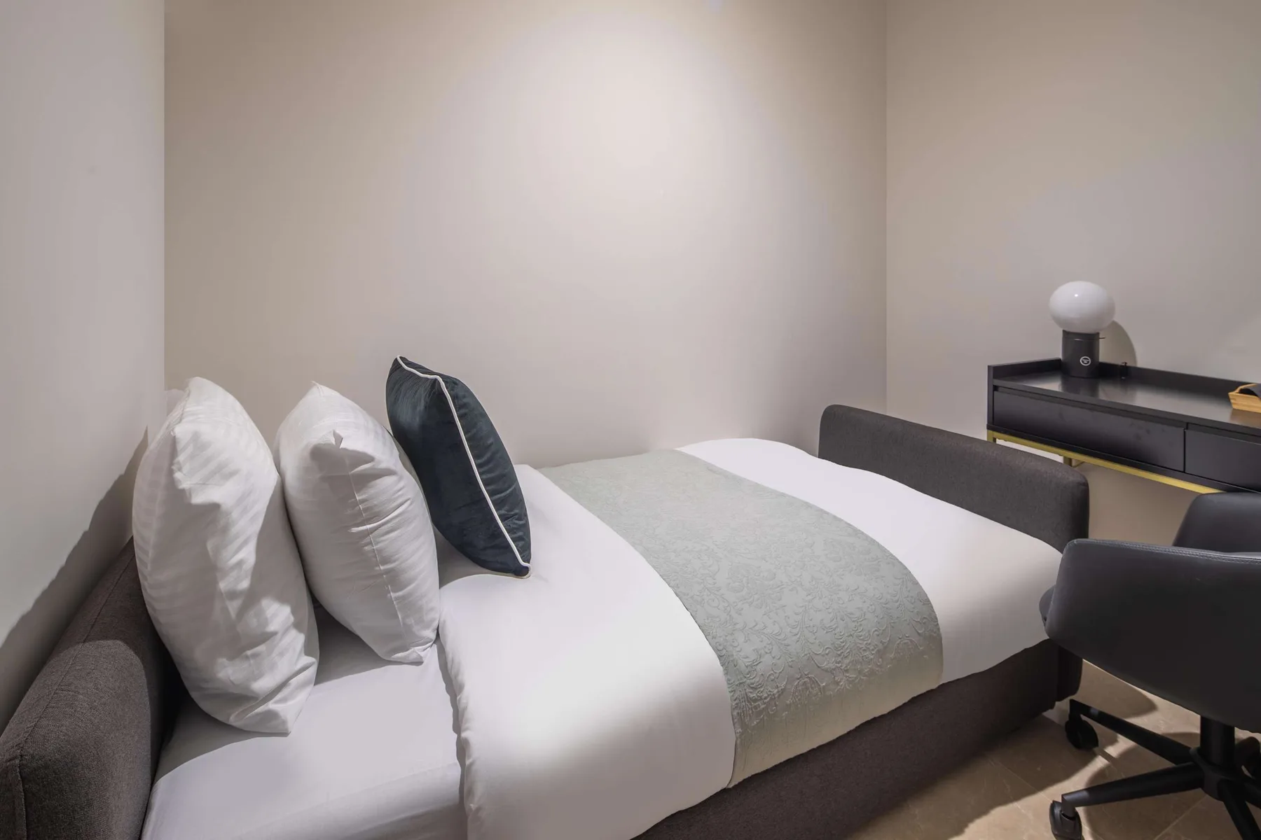 Un dormitorio con una cama bien tendida y un escritorio con una silla.