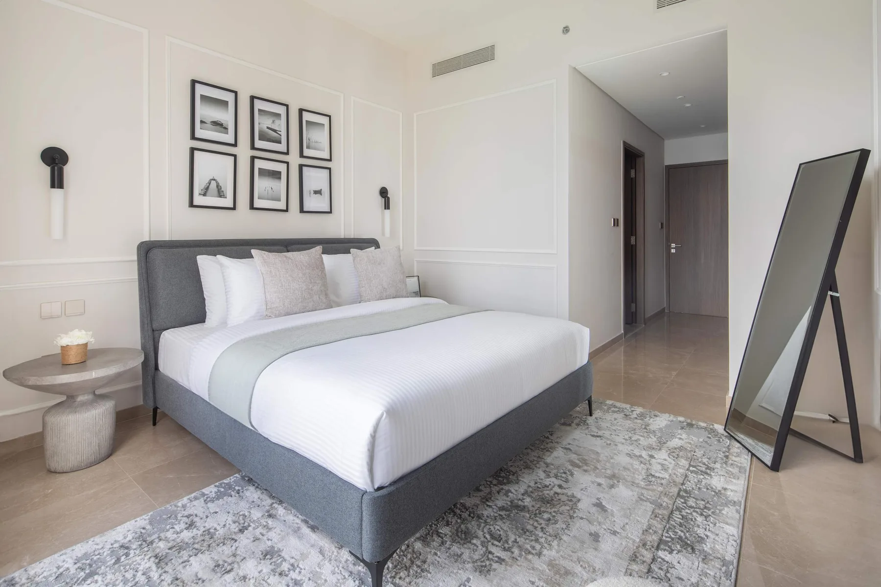 Un dormitorio luminoso con una cama bien arreglada, cuadros enmarcados y una alfombra estampada.