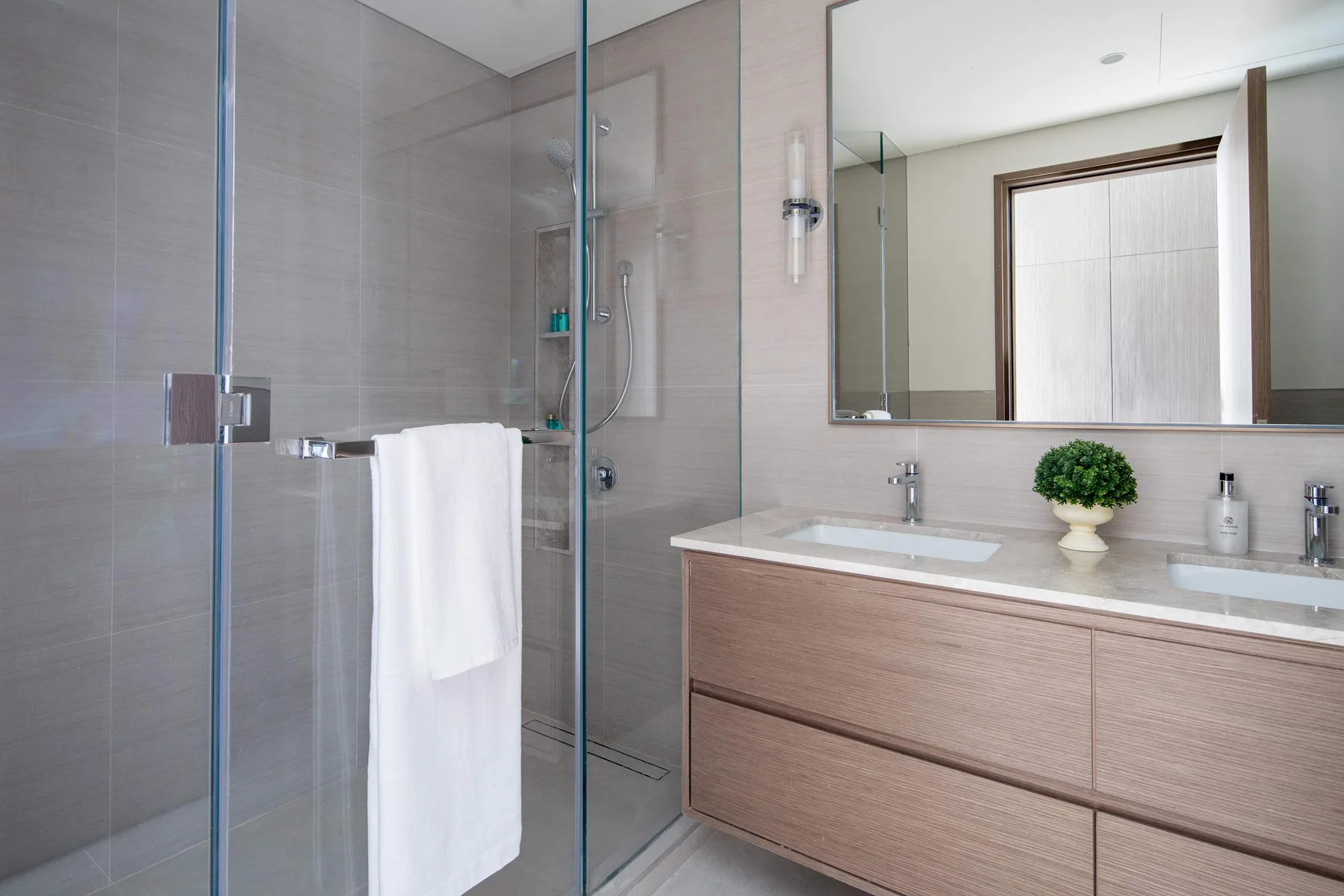 Un baño moderno con una ducha de vidrio y un tocador largo bajo un espejo.