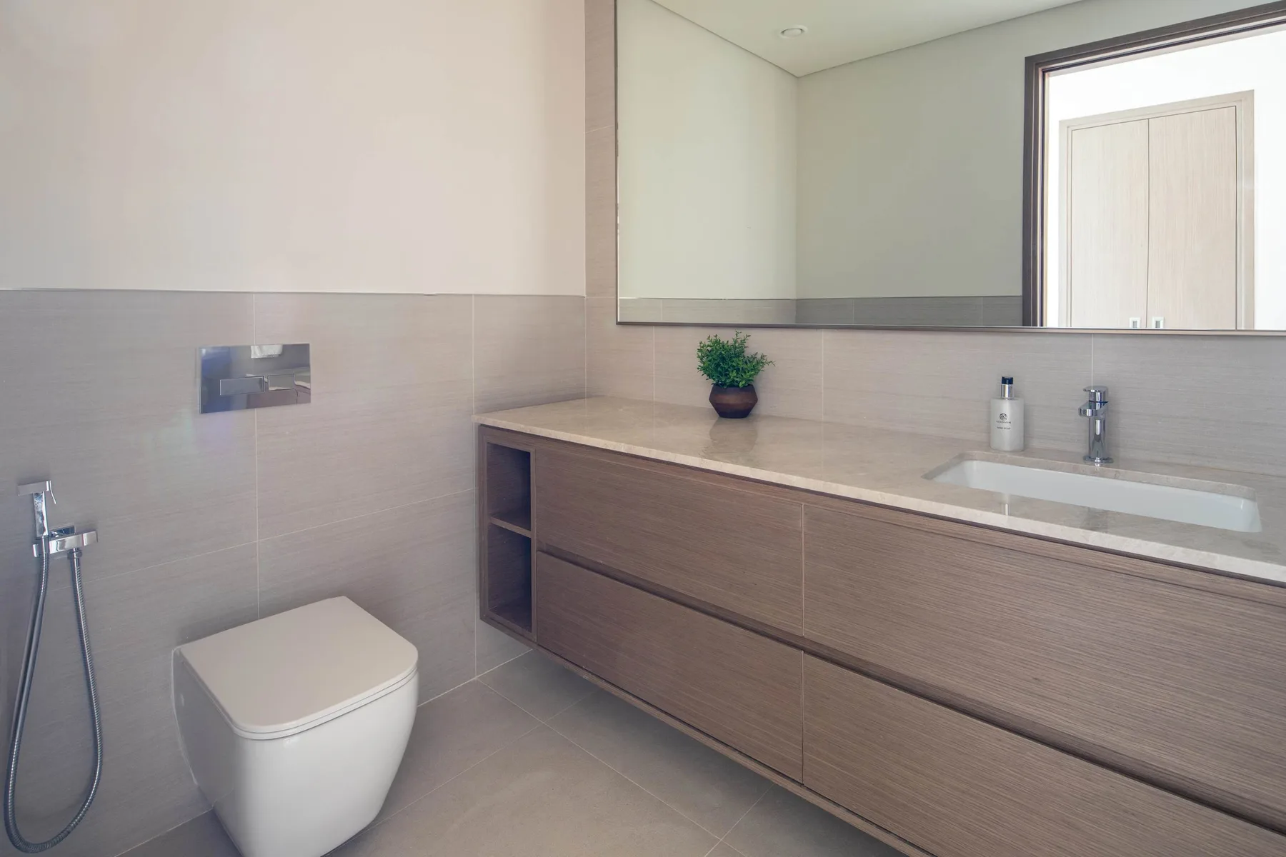 Un baño moderno con un inodoro y un largo mueble de lavabo bajo un espejo.
