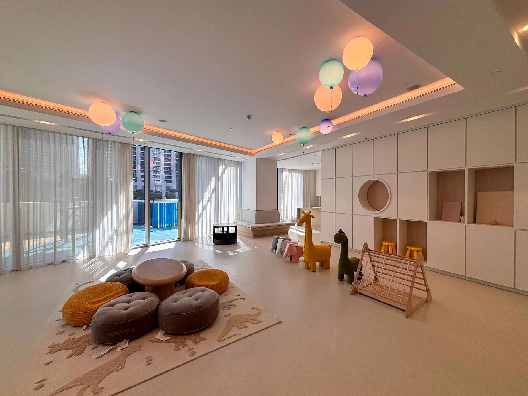 Una luminosa sala de juegos tiene cojines en el suelo, una mesa pequeña y luces colgantes de colores.