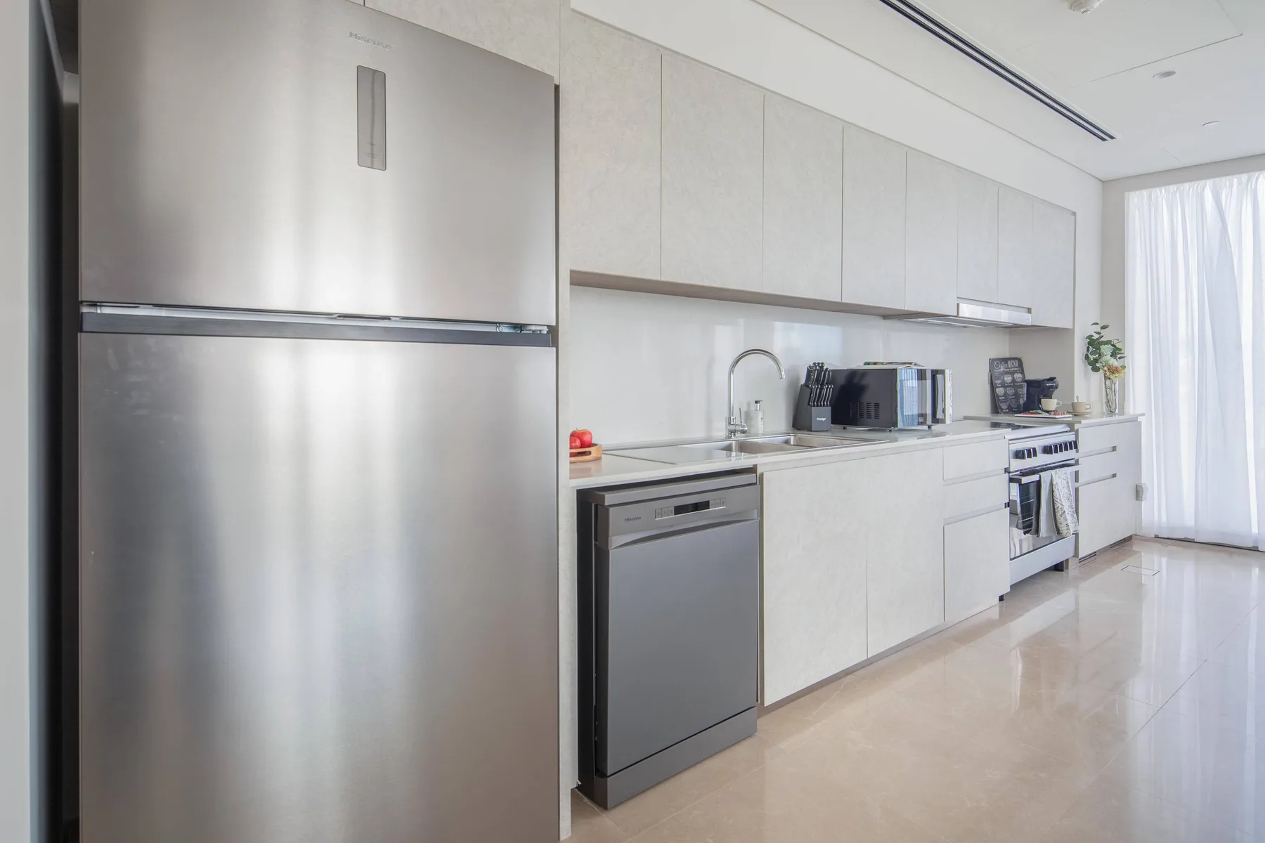 Una cocina moderna y luminosa con gabinetes blancos y electrodomésticos de acero inoxidable.