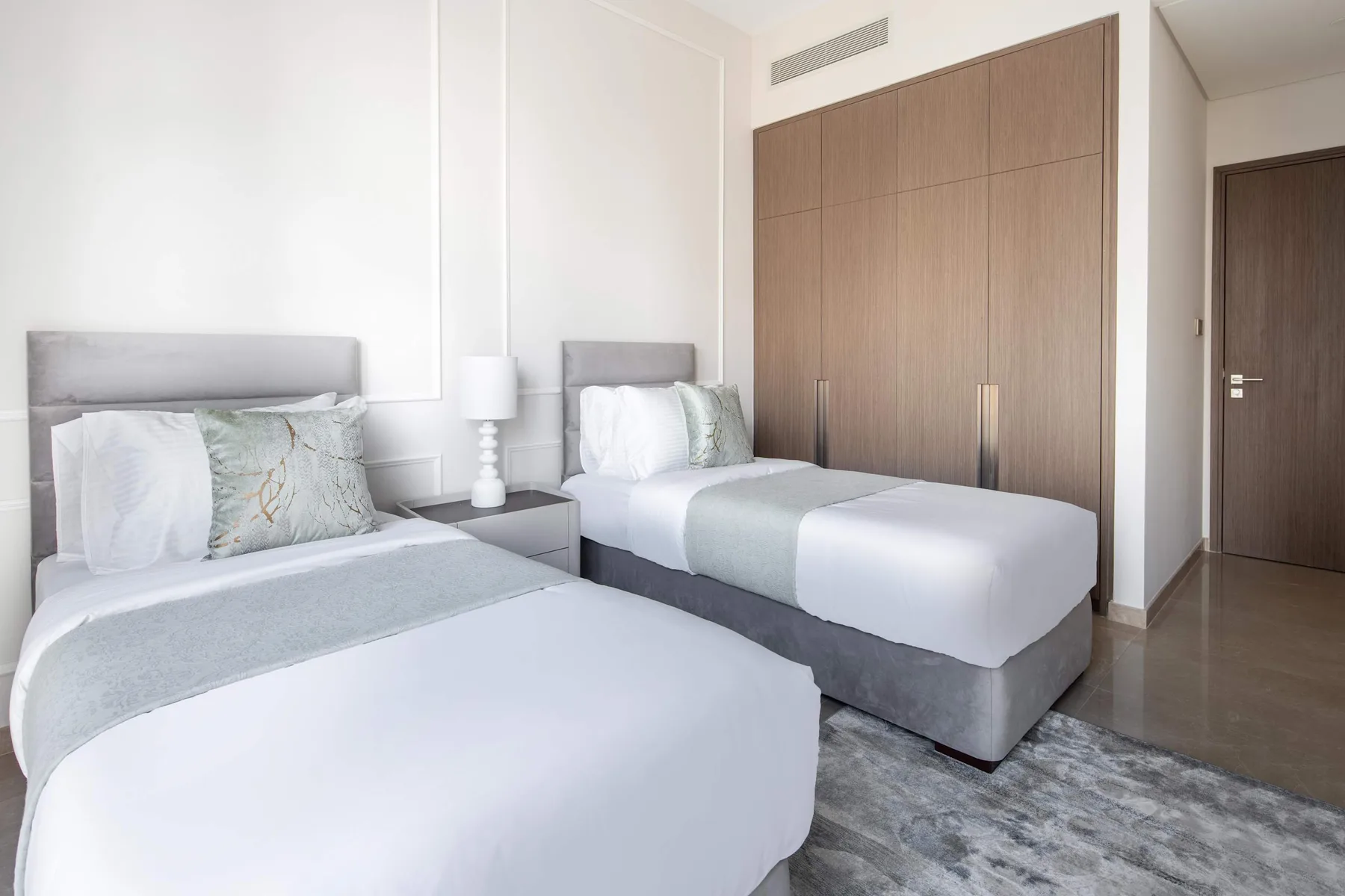 Un dormitorio luminoso con dos camas individuales, ropa de cama clara y un armario grande de madera.