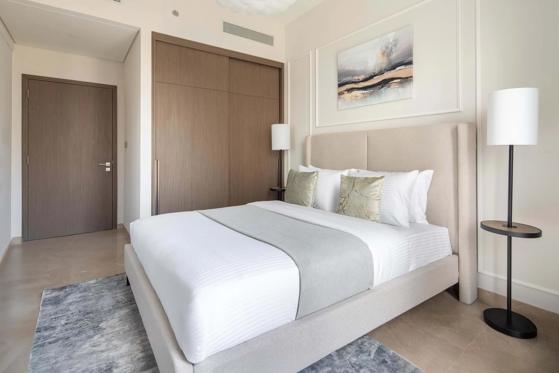 Un dormitorio luminoso con una cama bien tendida y una obra abstracta sobre el cabecero.