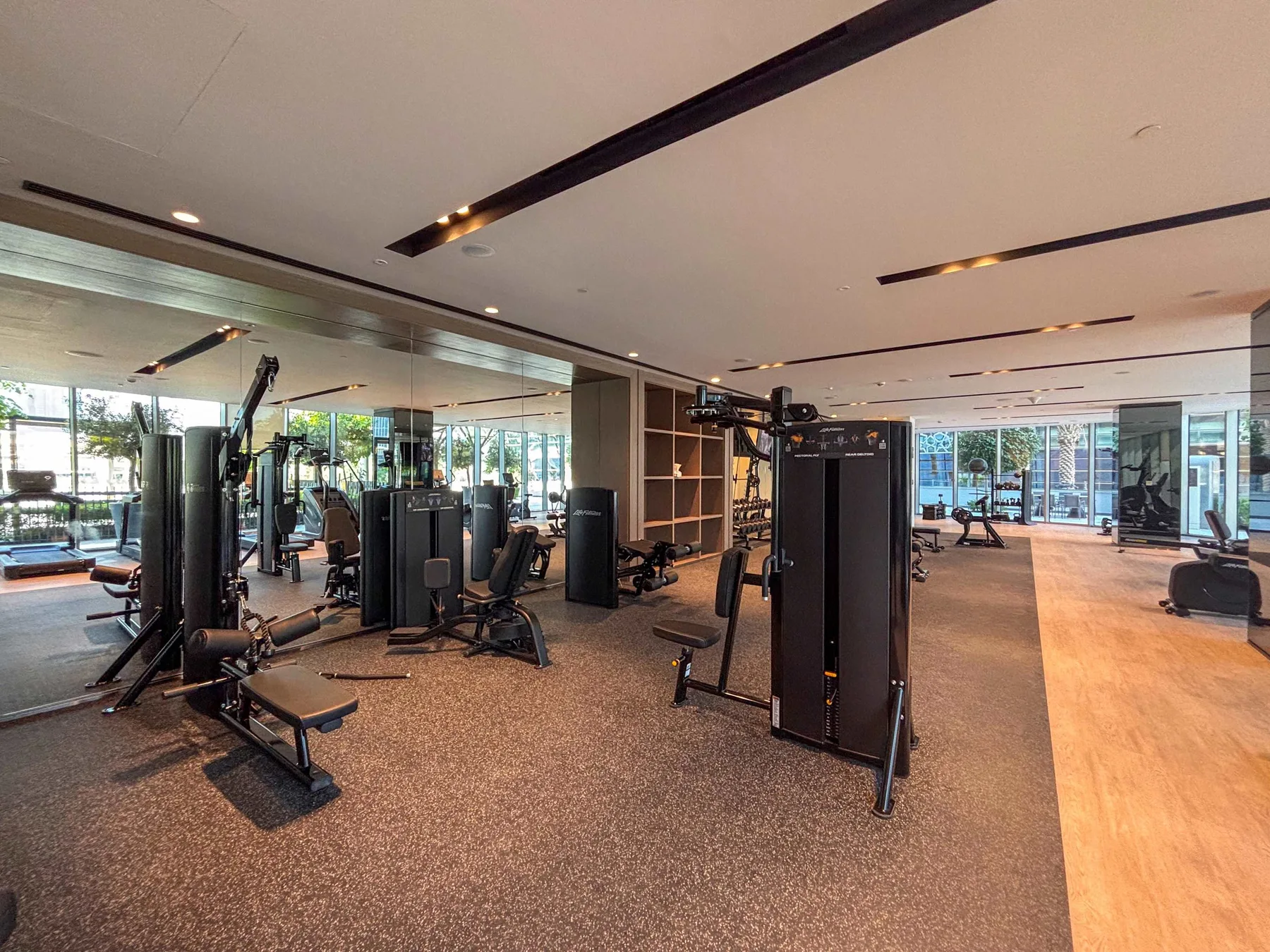 Un gimnasio con máquinas de ejercicio y grandes ventanas.