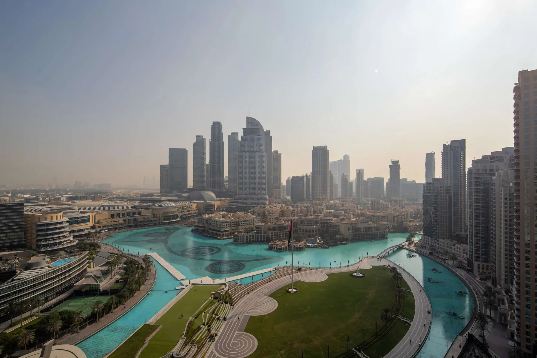 El horizonte urbano se alza sobre un canal turquesa y una zona verde ajardinada.