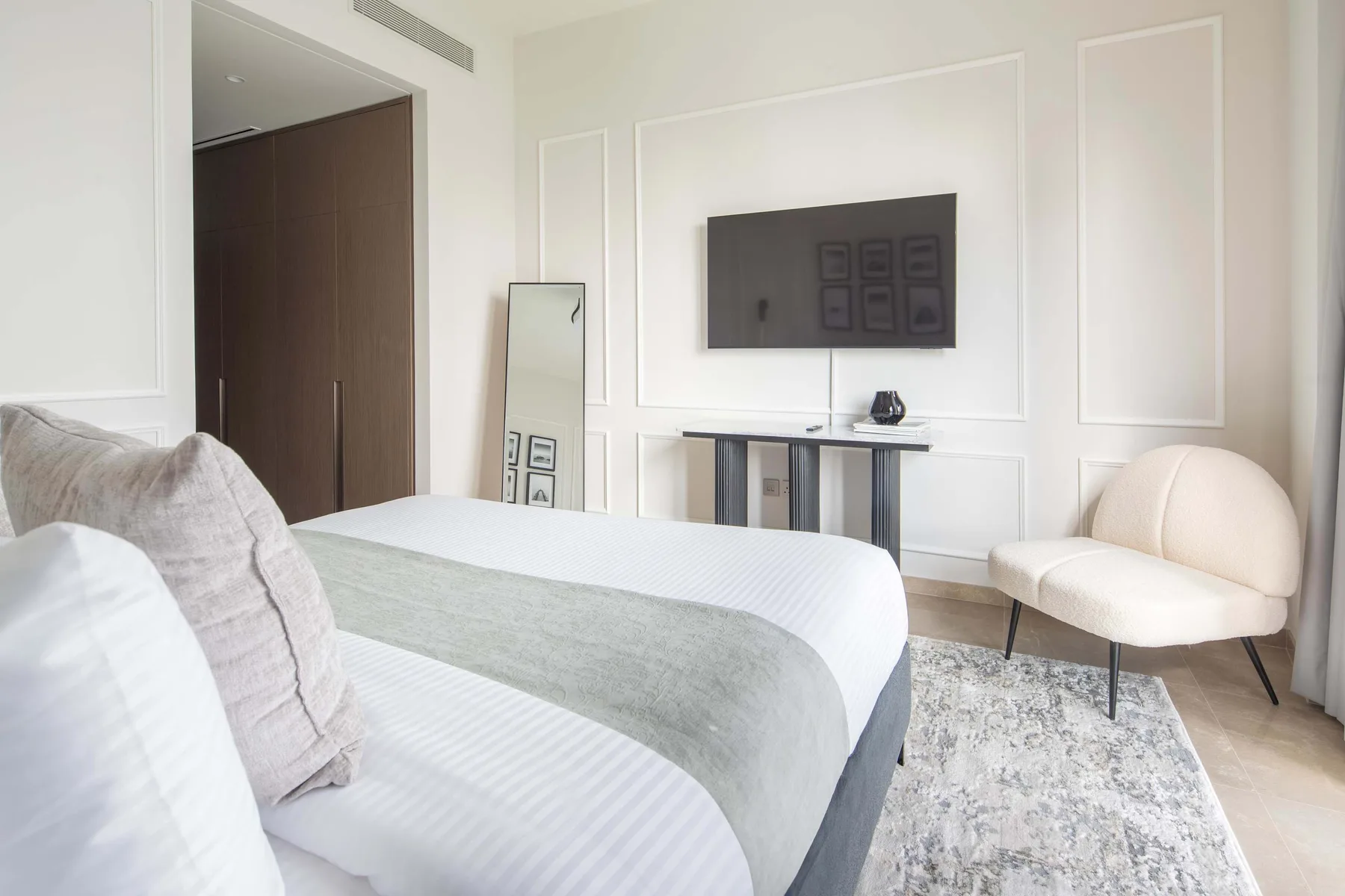 Un dormitorio con una cama, un televisor en la pared y una silla clara.