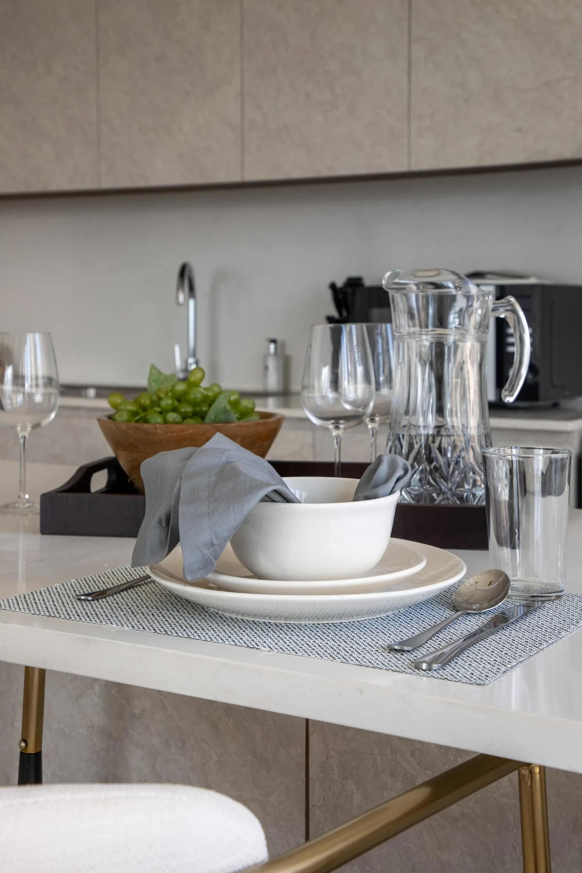 Una mesa de comedor está puesta con platos, copas y un cuenco de fruta verde.