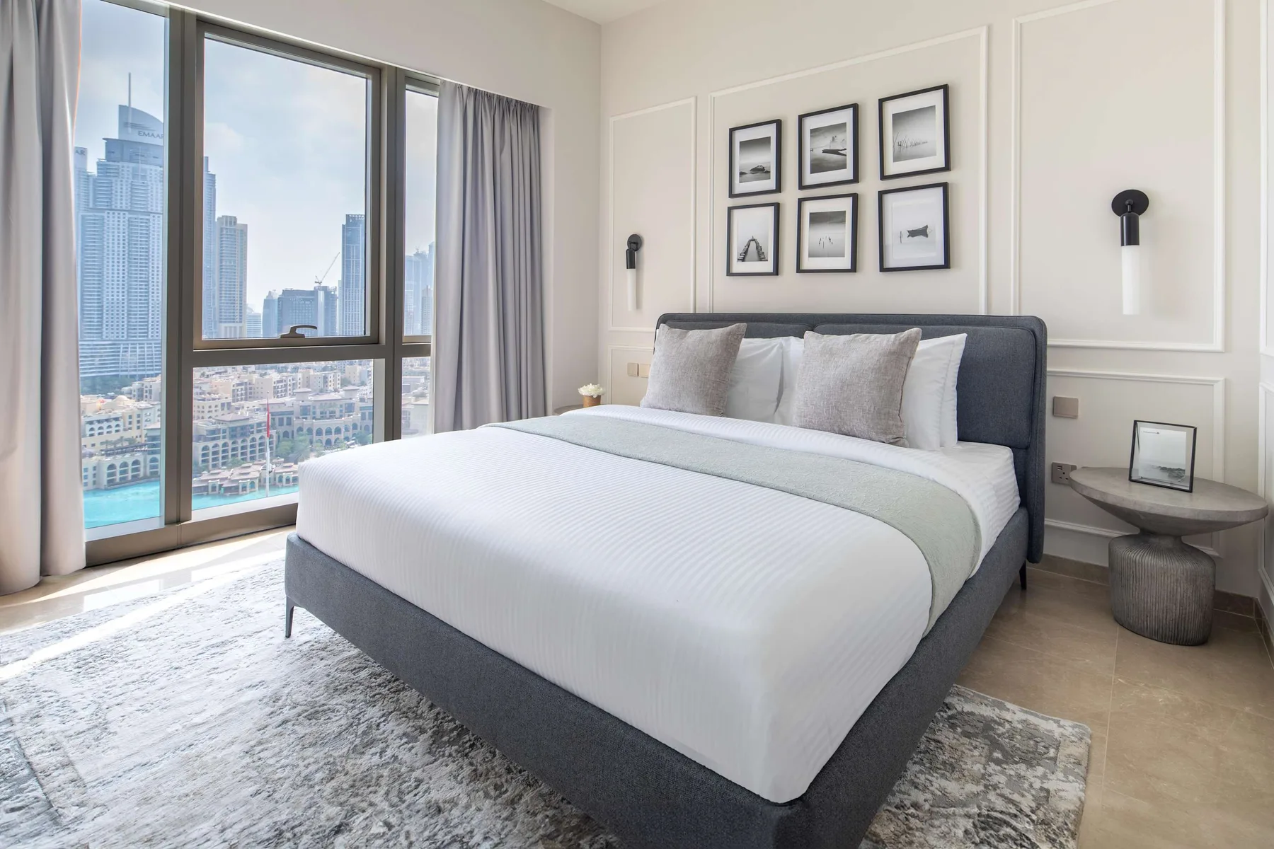 Dormitorio con una cama bien tendida, cuadros en la pared y grandes ventanas.