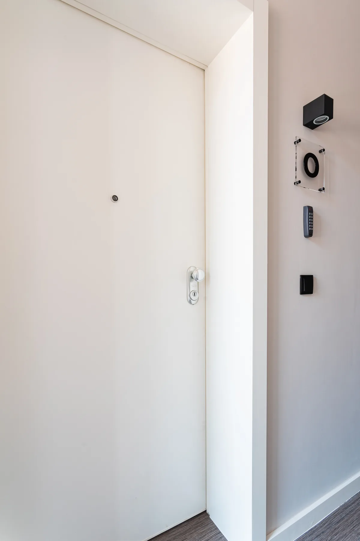 Una puerta de entrada blanca con mirilla y controles en la pared.