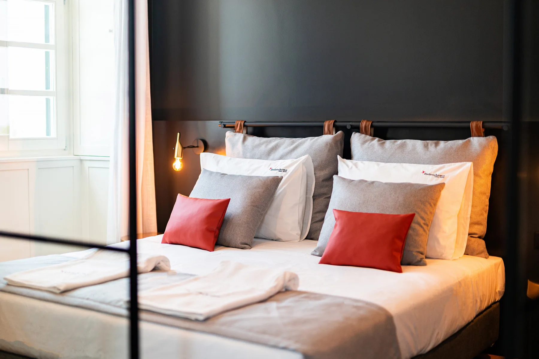 Dormitorio con una cama bien arreglada, varias almohadas y cojines rojos.