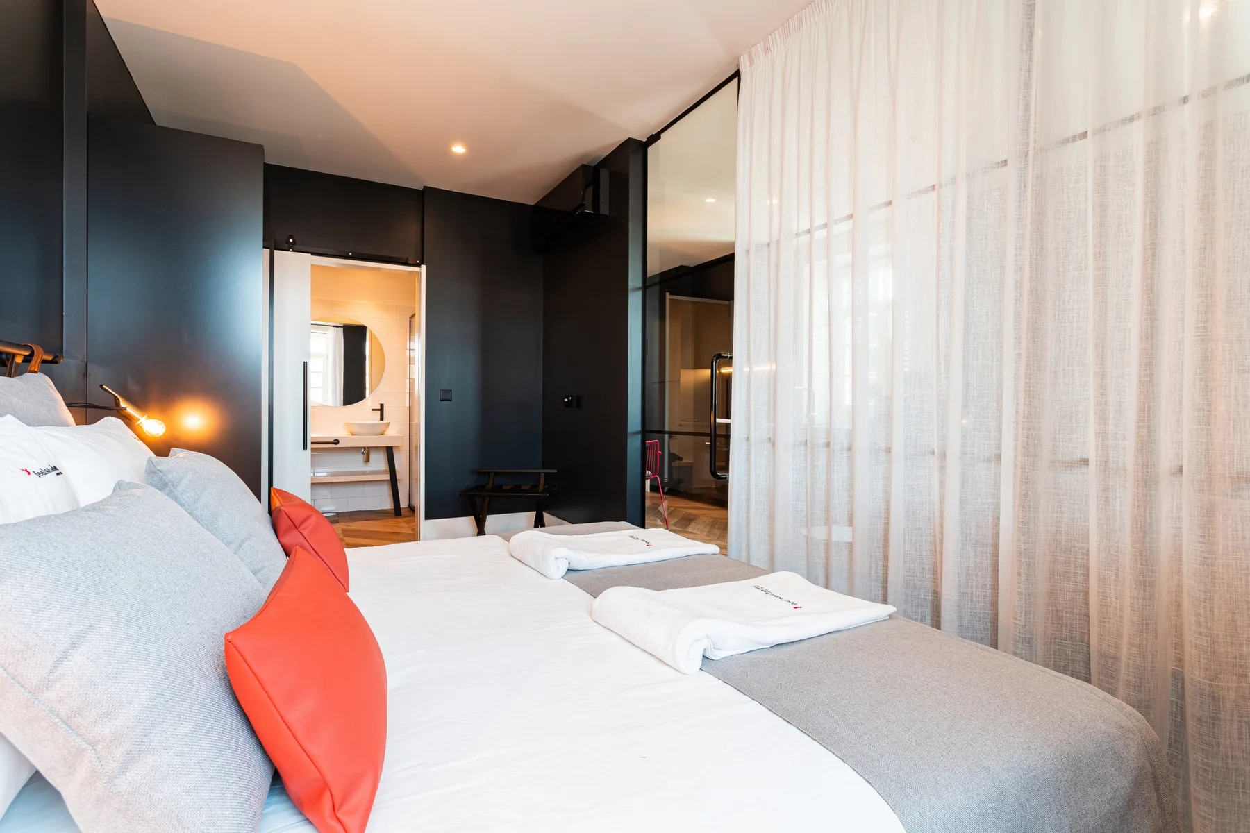 Dormitorio con una cama, toallas dobladas y cortinas translúcidas.