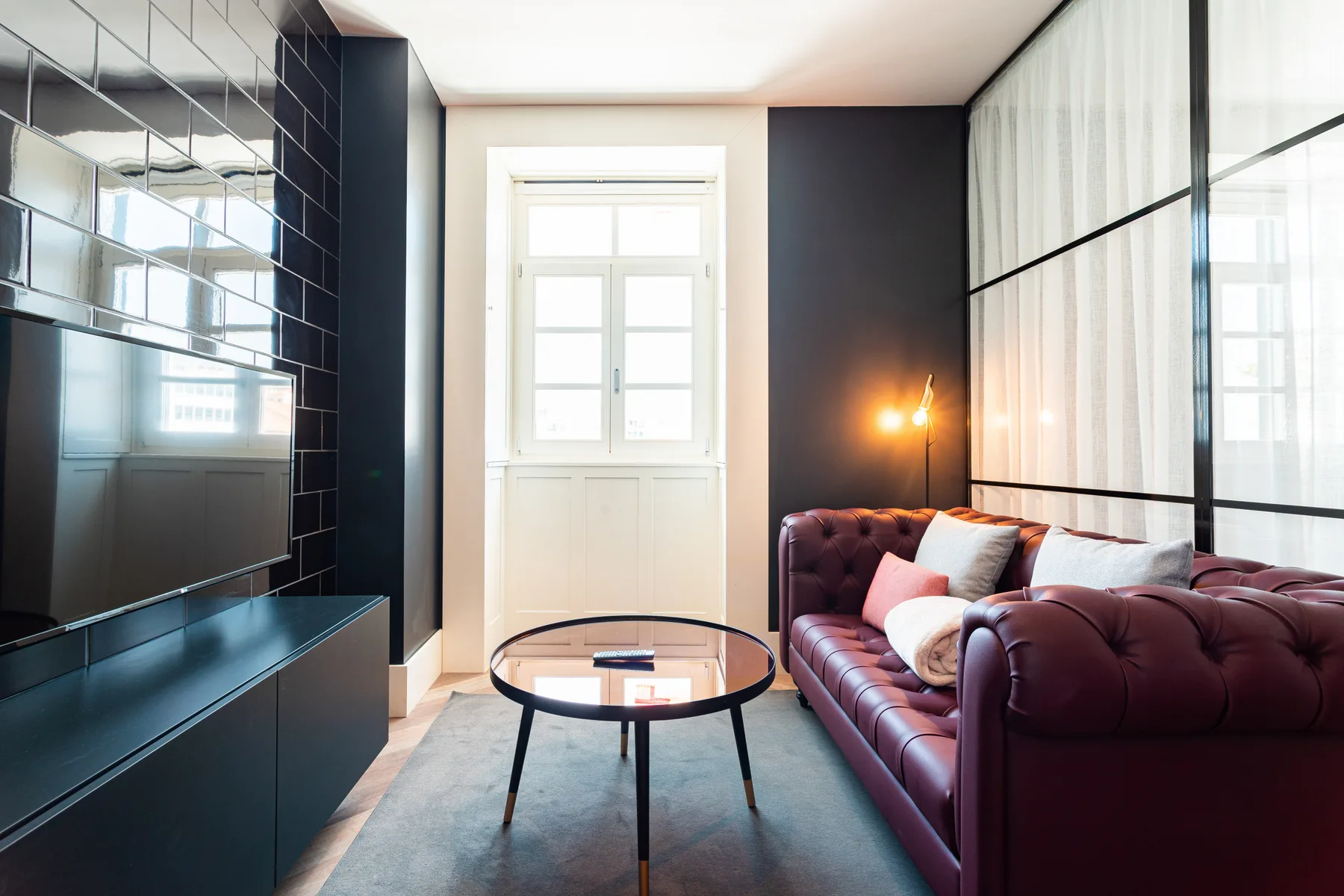A living room with a burgundy sofa, glass coffee table, and wall-mounted television.