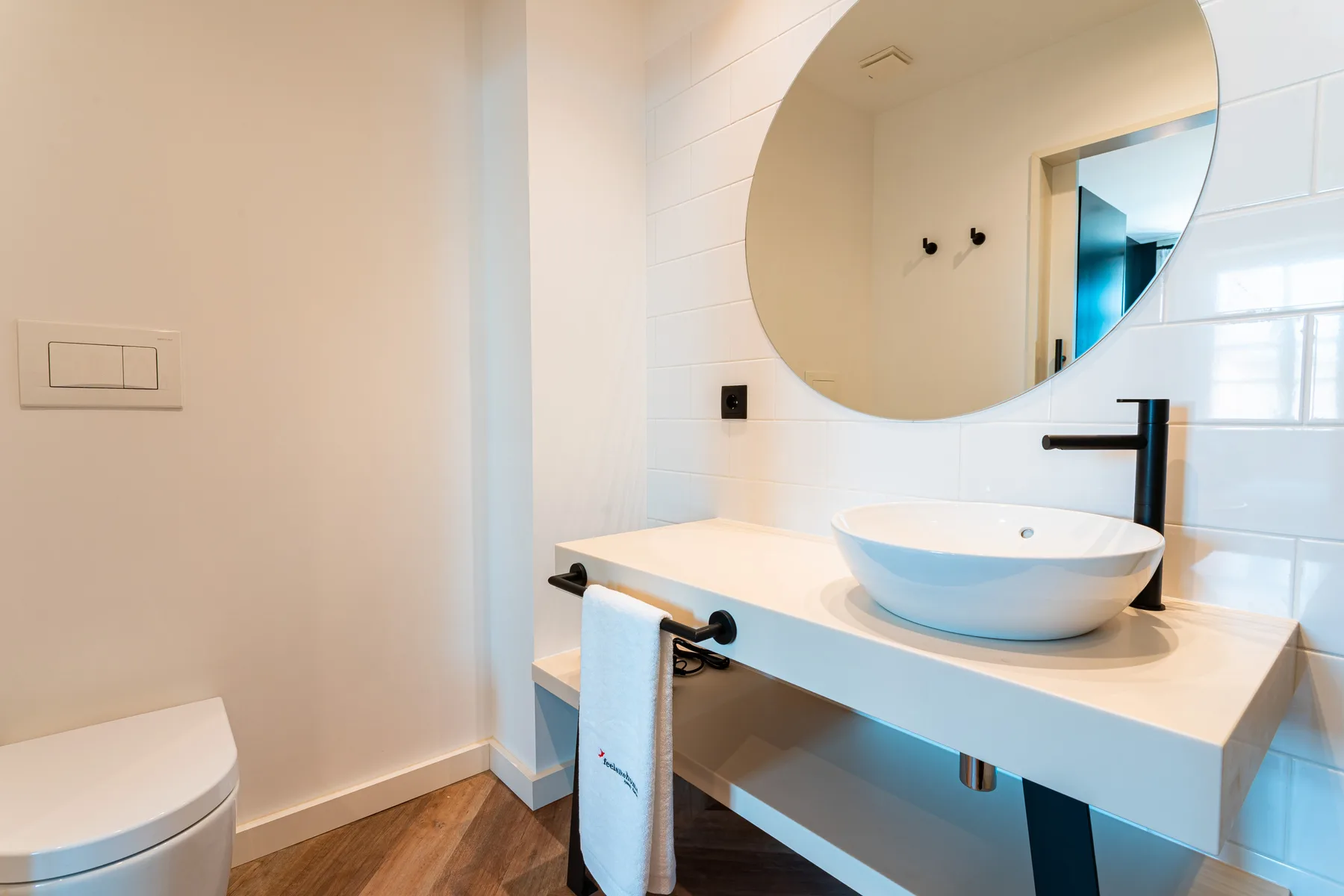 Un lavabo de baño con un lavamanos sobre encimera y un espejo redondo grande.