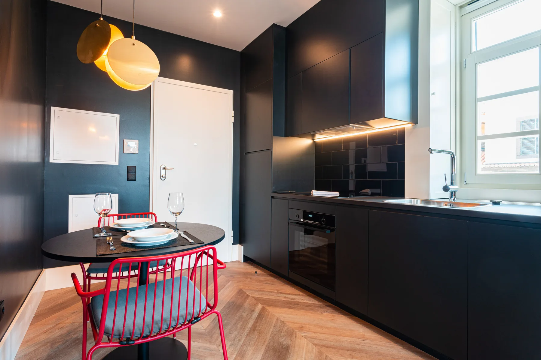 Cocina y comedor modernos con armarios oscuros y una silla roja.