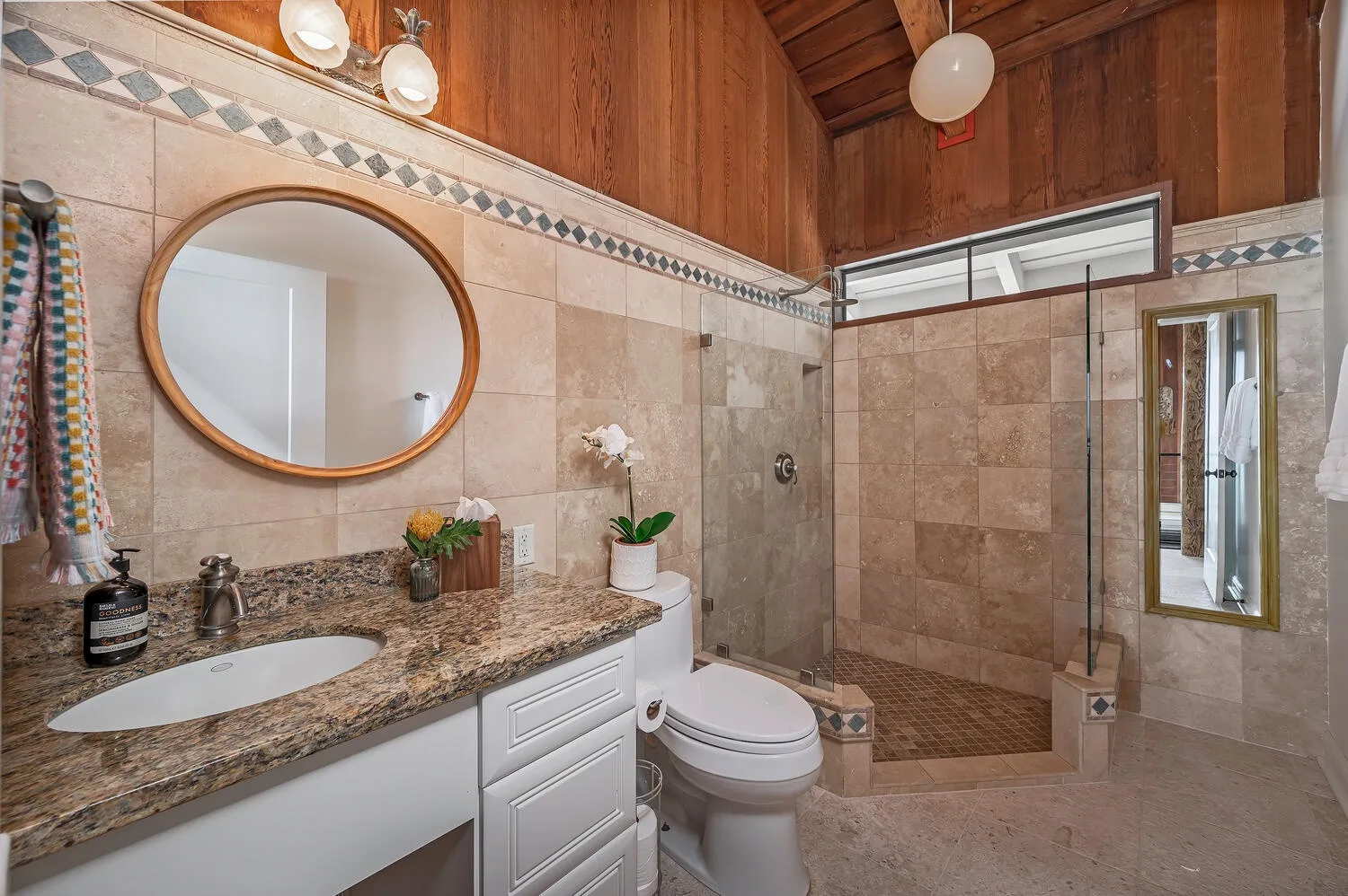 A tiled bathroom with a vanity, toilet, and glass shower.