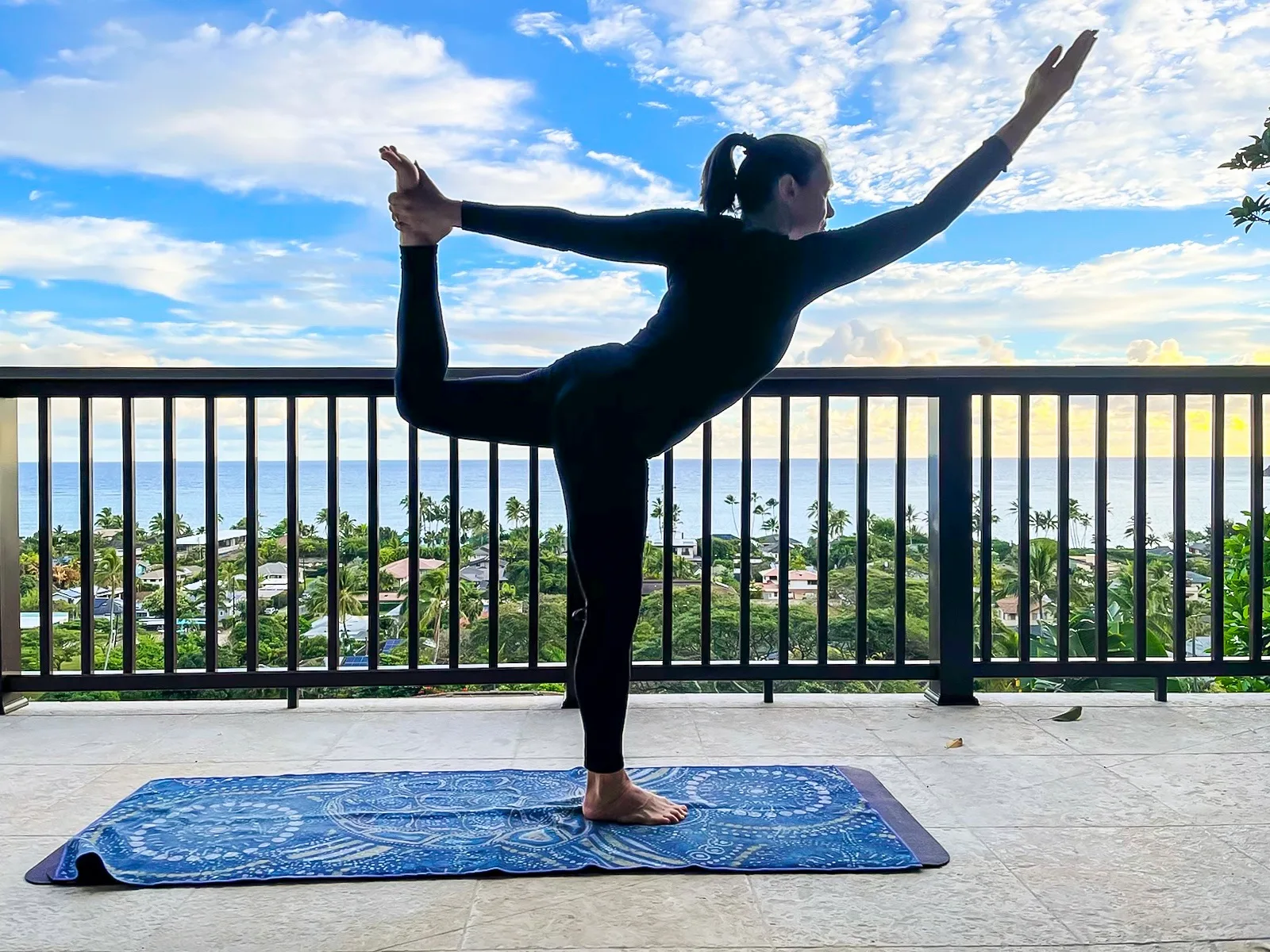 A person balances in a yoga pose on a mat beside a balcony railing.