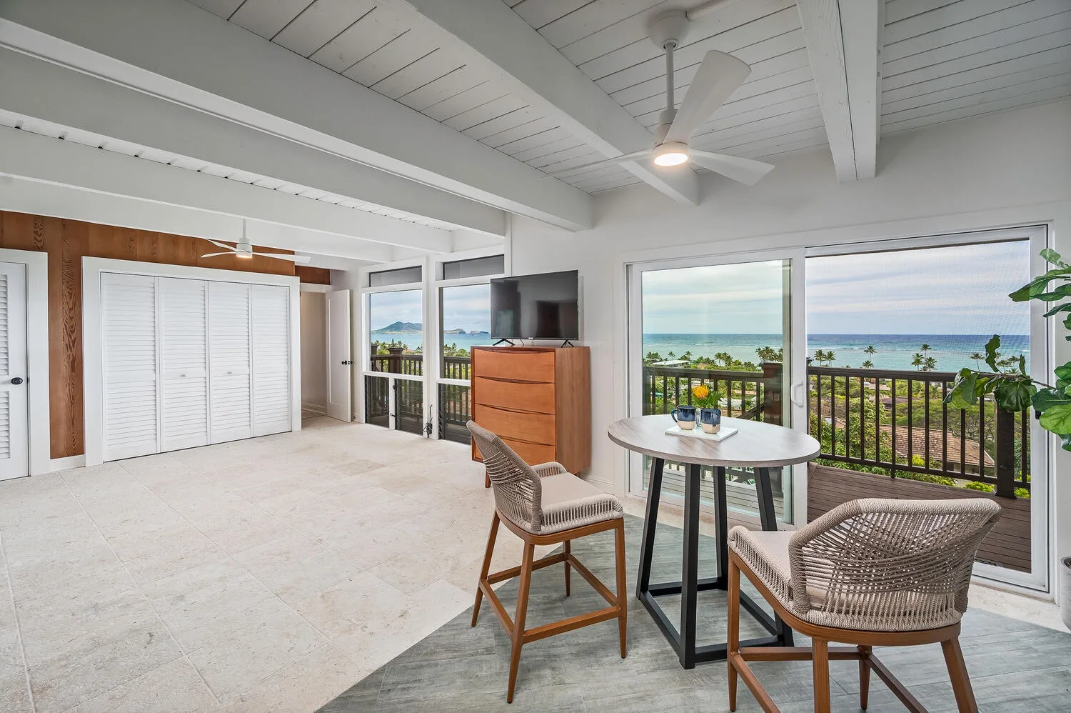 A bright sitting area with a round table and ocean views through glass doors.