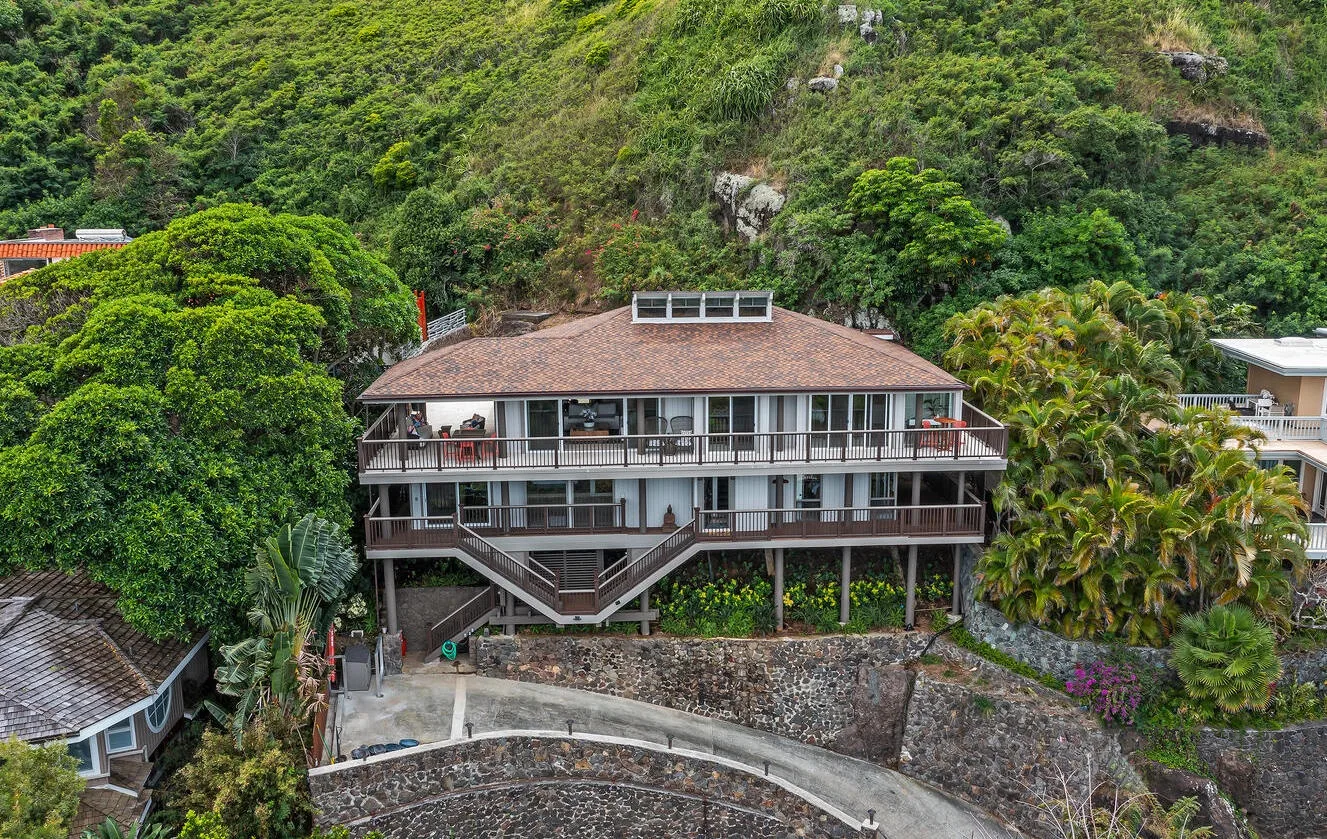 A large house with broad balconies sits against a densely vegetated hillside.