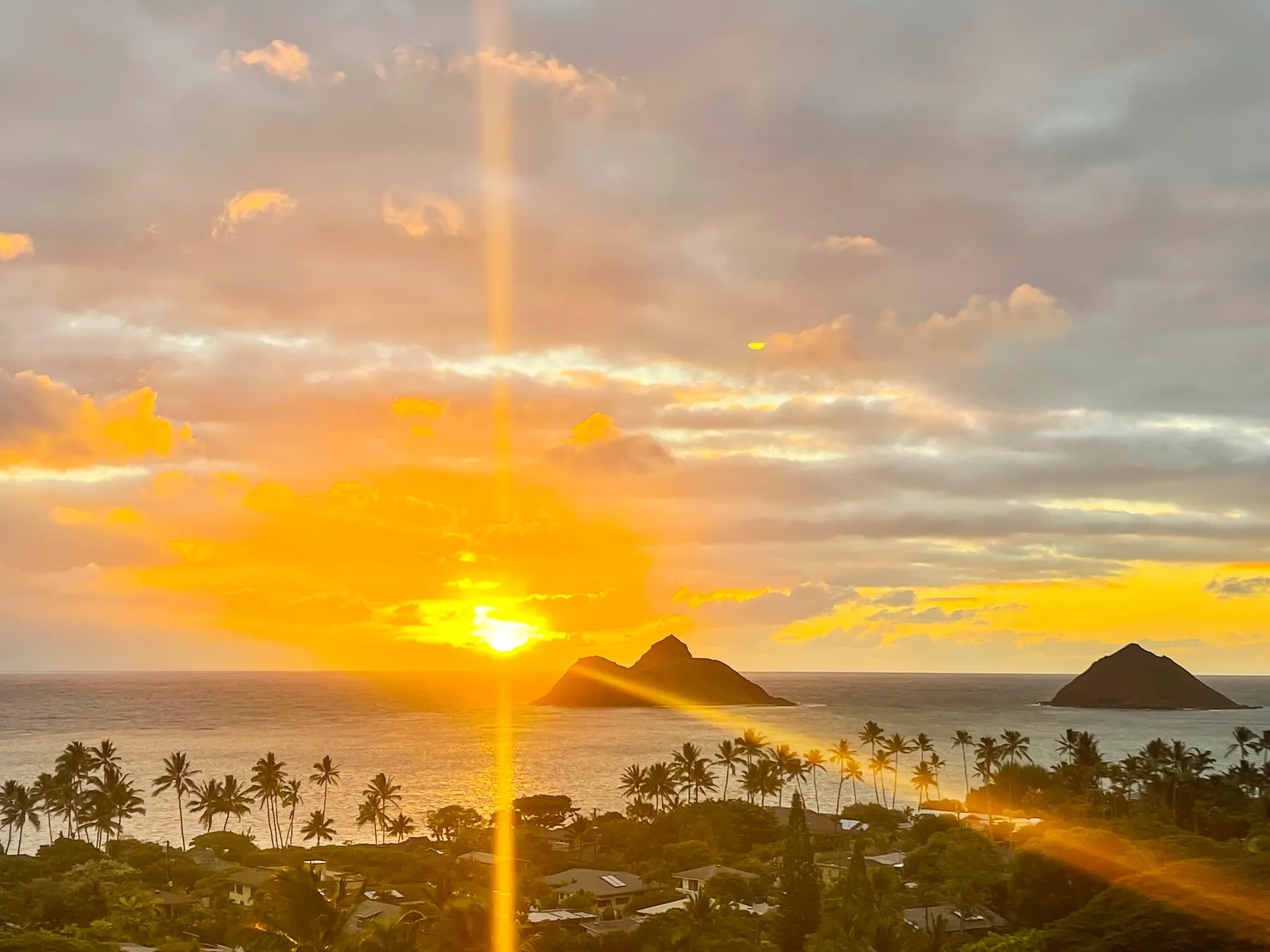 A coastal landscape at sunset, with palm trees and small islands on the horizon.