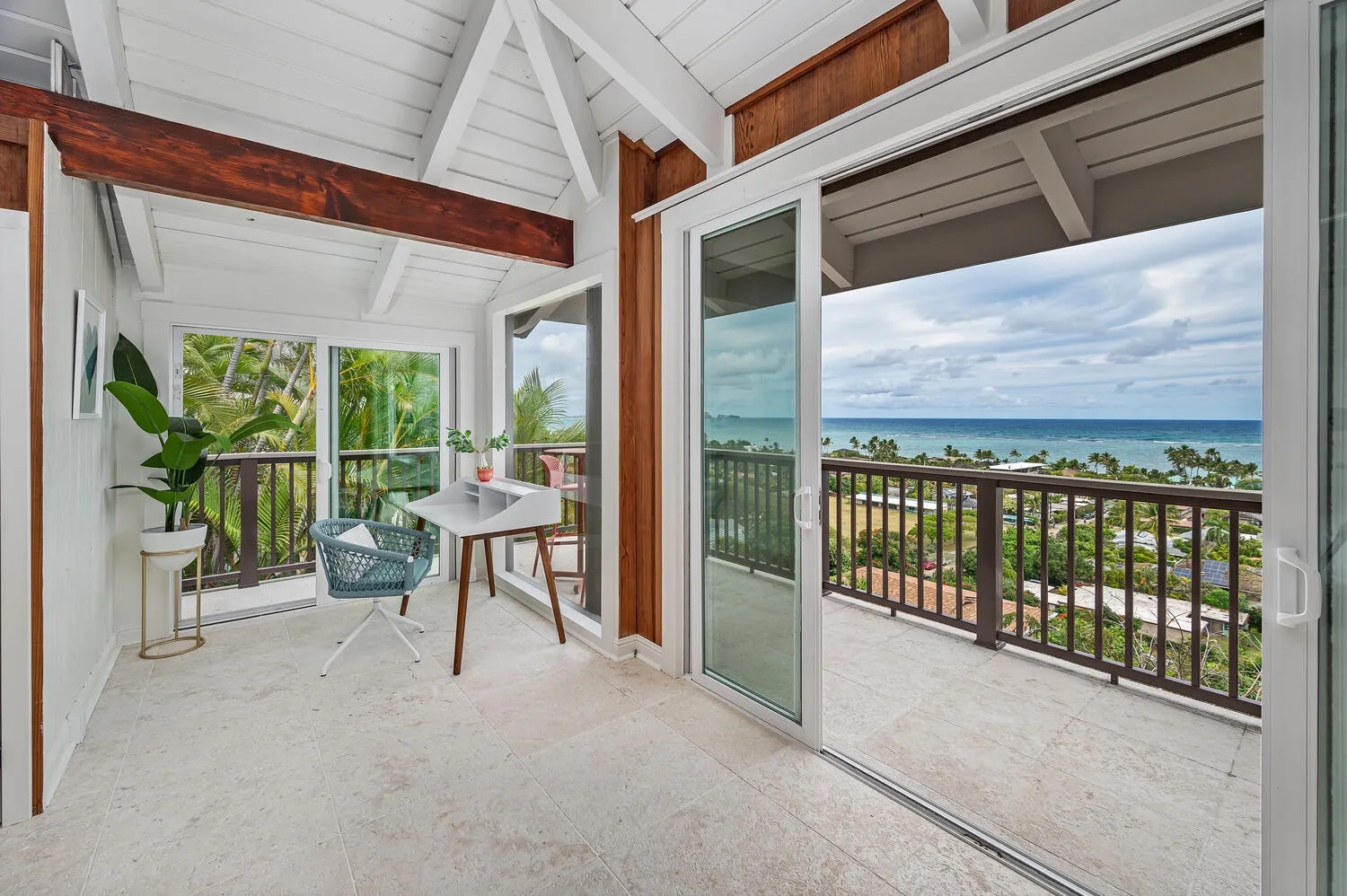 A bright room opens onto a balcony with a view of the ocean.