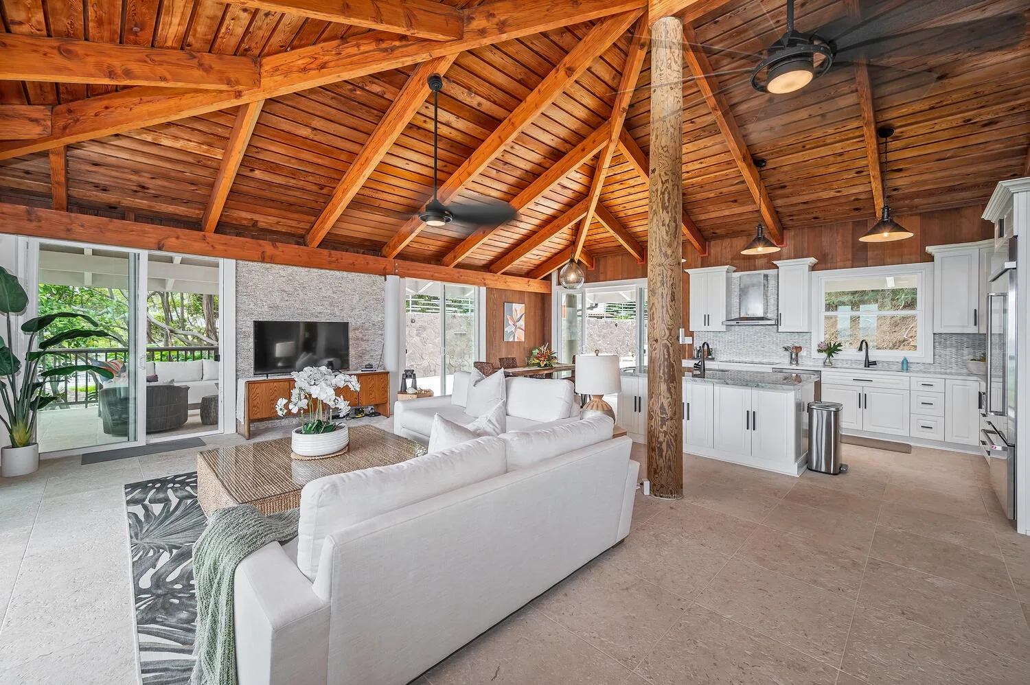 An open living room and kitchen beneath a high wooden ceiling.