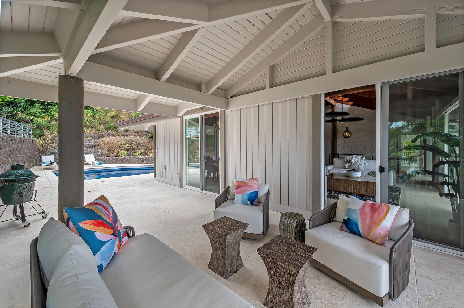 A covered patio with cushioned seating overlooks a swimming pool.