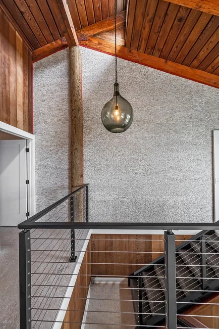 An interior stairwell with a wooden ceiling, pendant light, and metal railing.