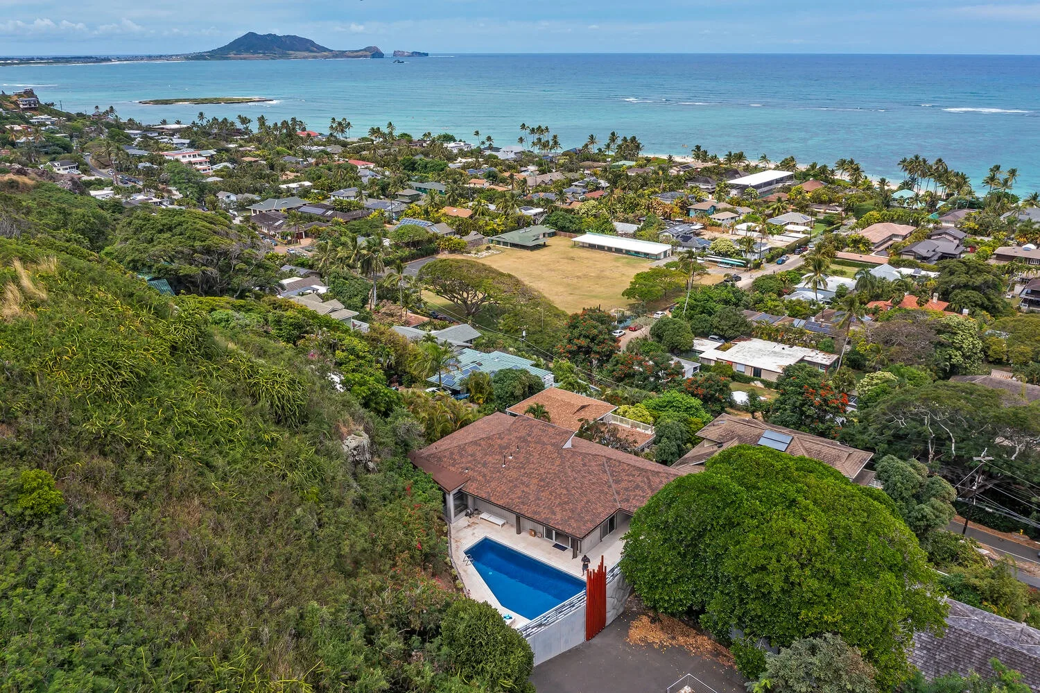 A hillside neighborhood overlooks the coastline, with a house and pool in the foreground.