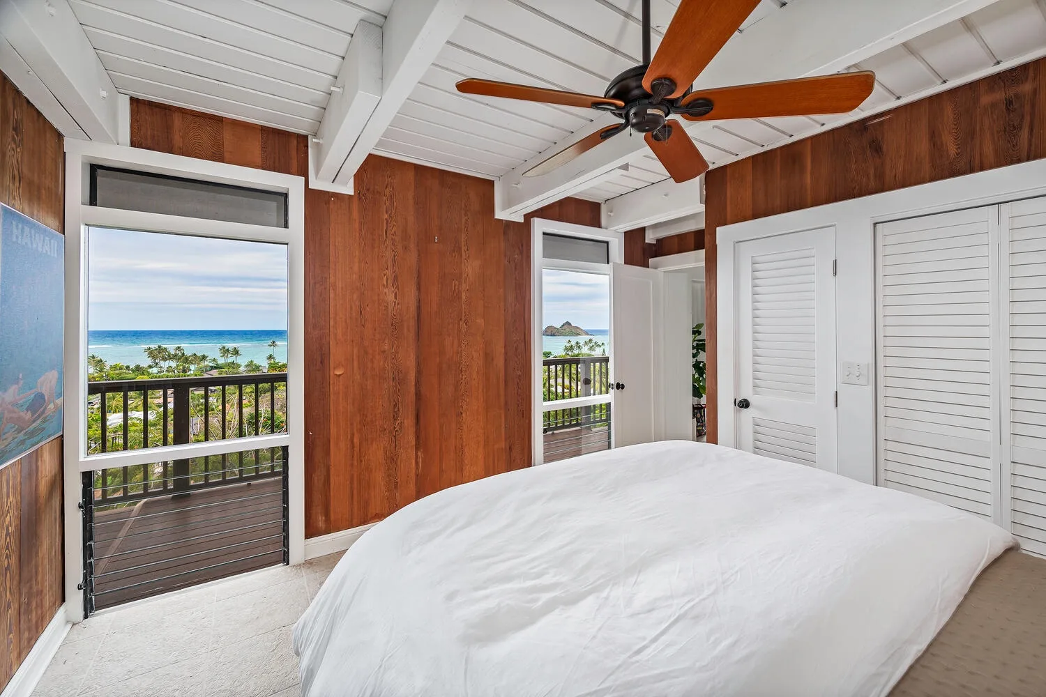 A bedroom with a large bed, wooden walls, and balcony doors overlooking the ocean.