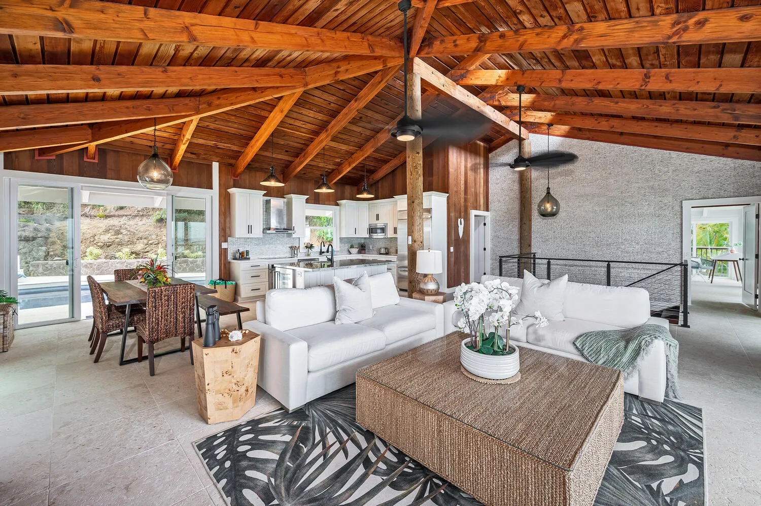 An open-plan living room with white seating, a dining area, and a wood-beamed ceiling.