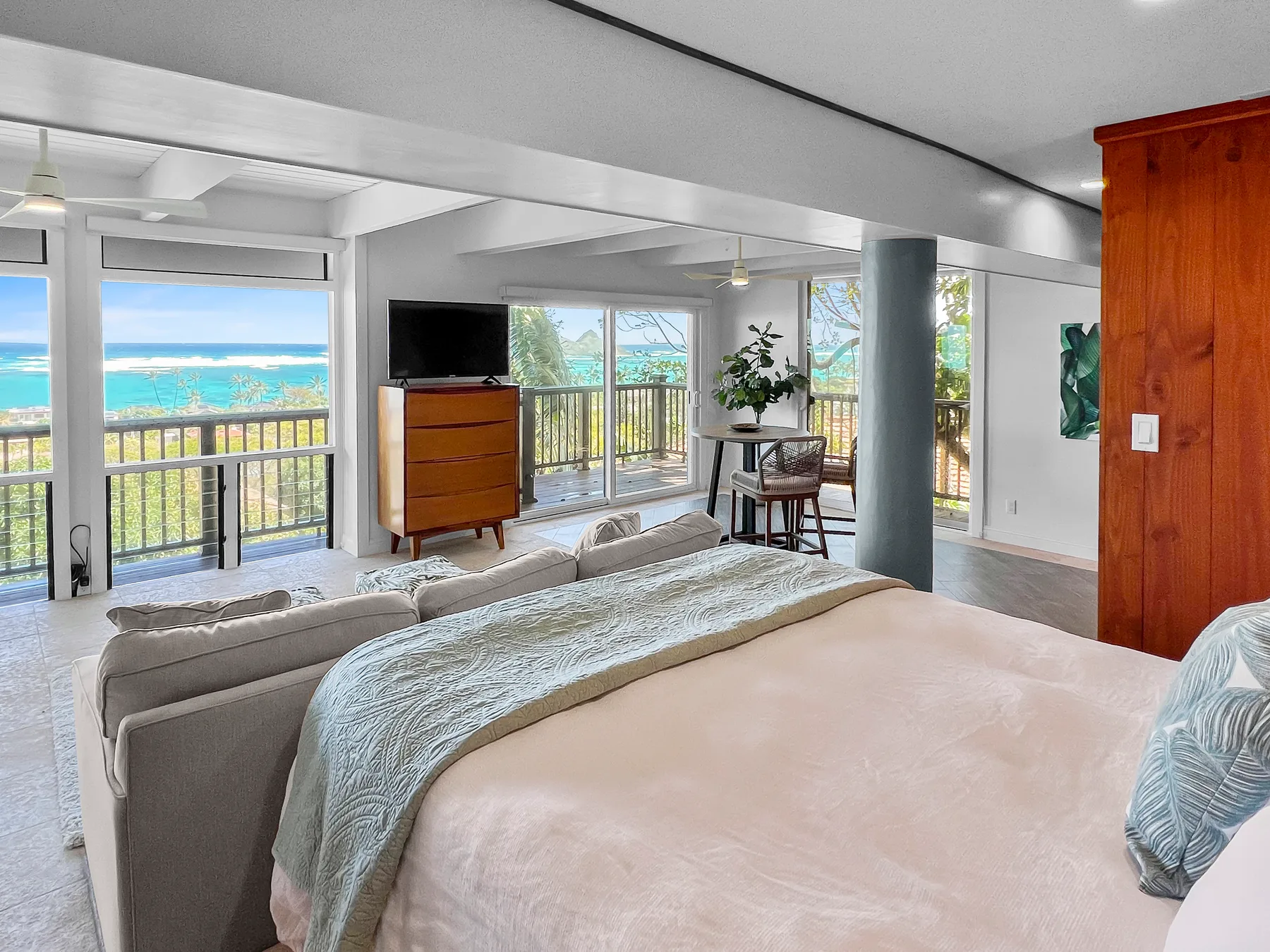 A bedroom opens into a living area with large windows overlooking the ocean.