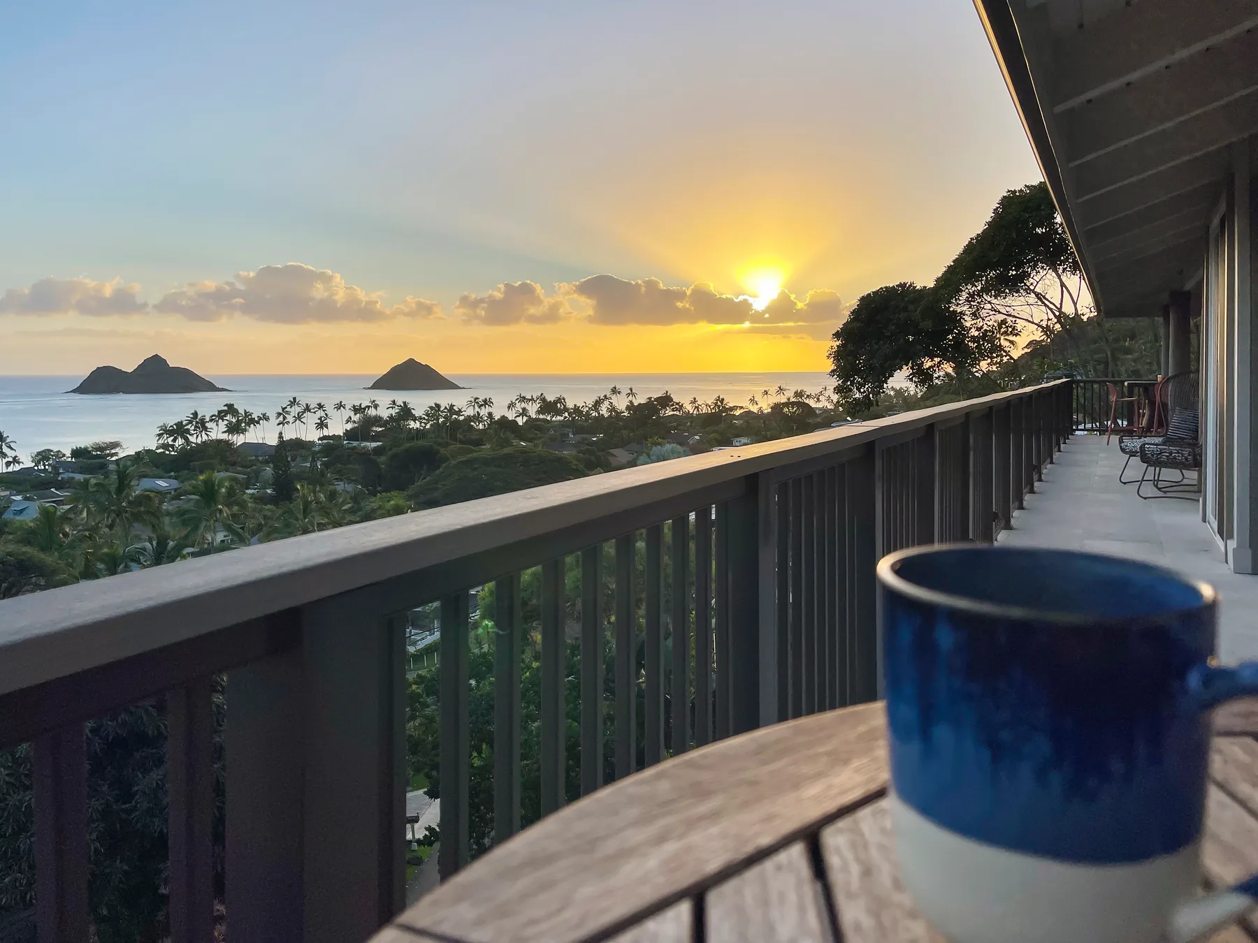 A balcony overlooks the ocean and distant islands at sunset.