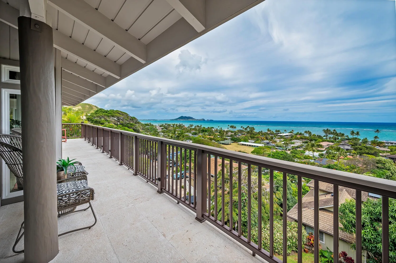 A covered balcony overlooks green rooftops and the ocean.