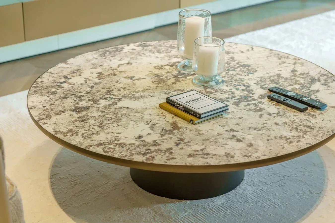 Una mesa de centro redonda tiene dos velas, un libro y controles remotos.