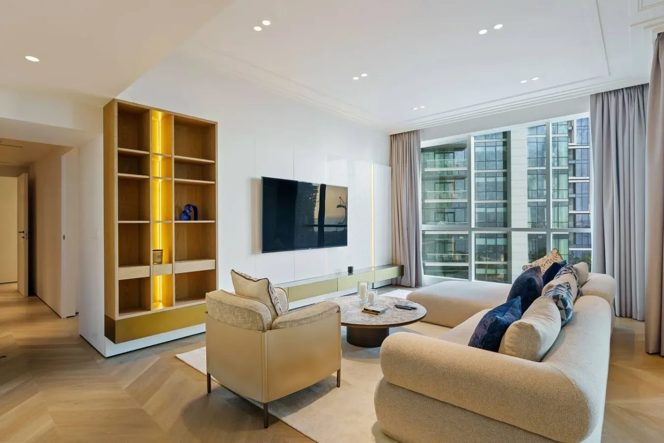 Una sala luminosa con asientos claros, un televisor y grandes ventanas.
